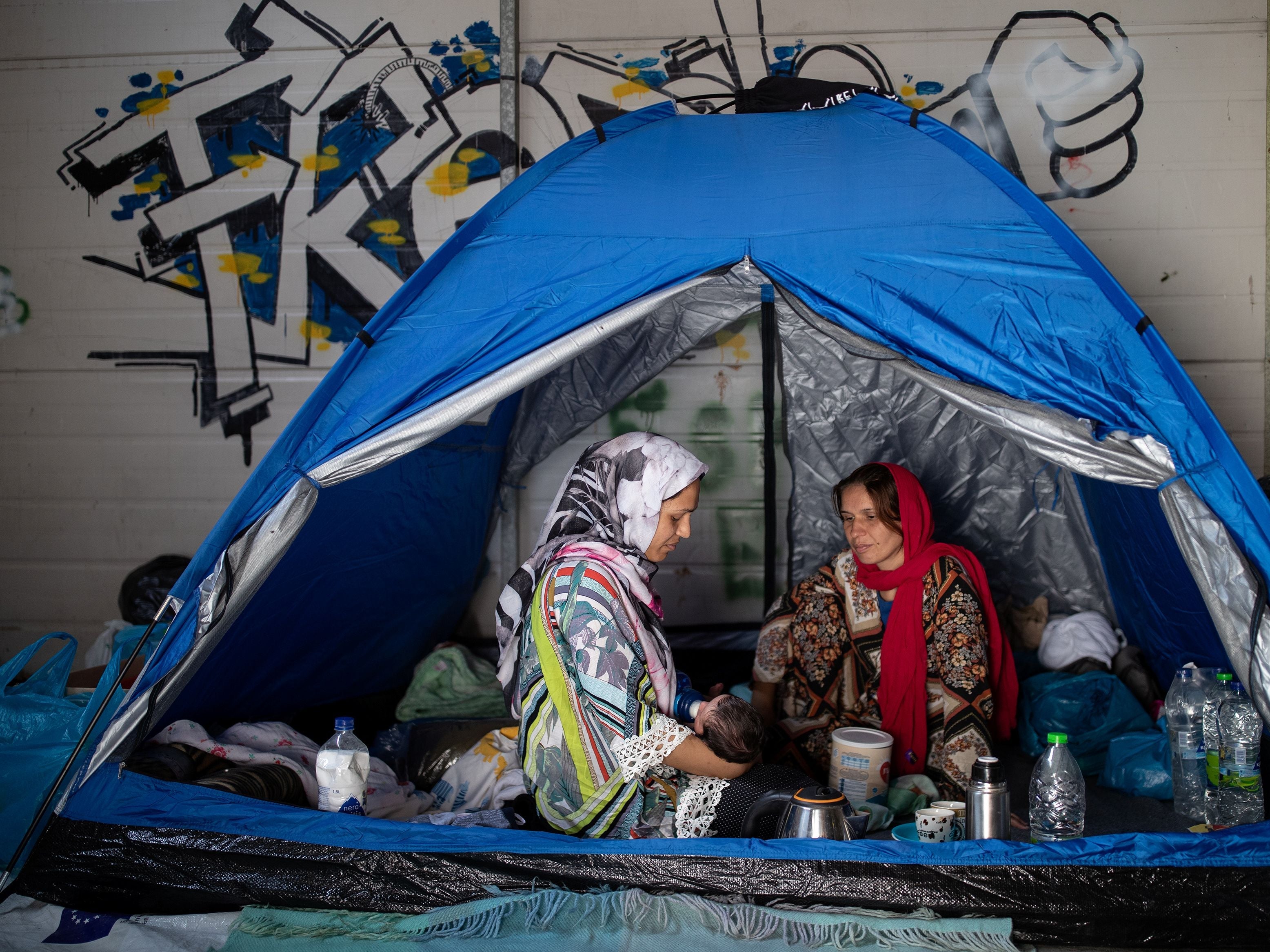 A woman gives milk to her newborn baby as refugees and migrants from the destroyed Moria camp find shelter in a warehouse near a new temporary camp, on the island of Lesbos, Greece