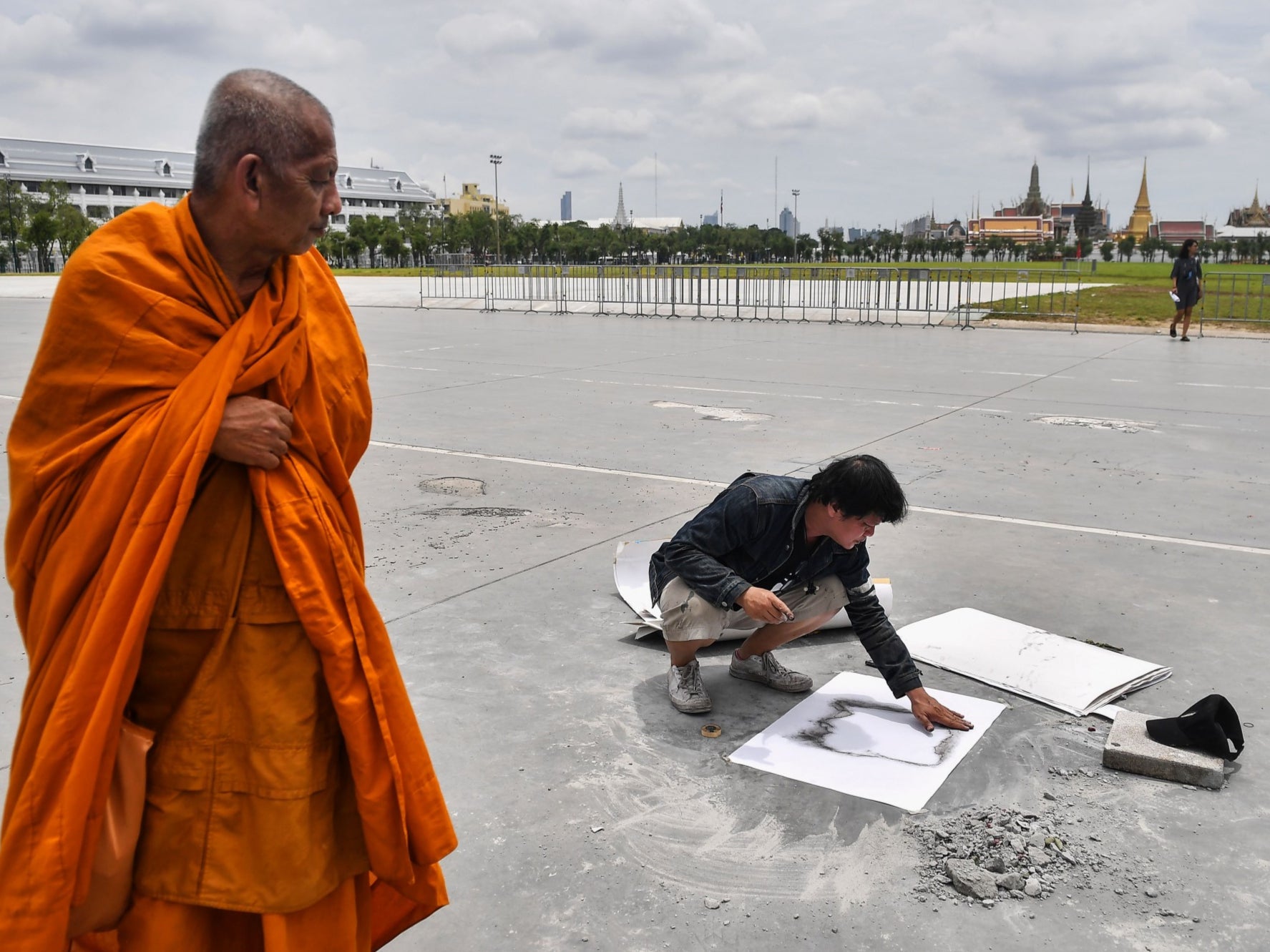 A monk watches as an art professor from Silpakorn University makes a stencil over an empty space in Bangkok where the commemorative plaque had been placed by pro-democracy protest leaders