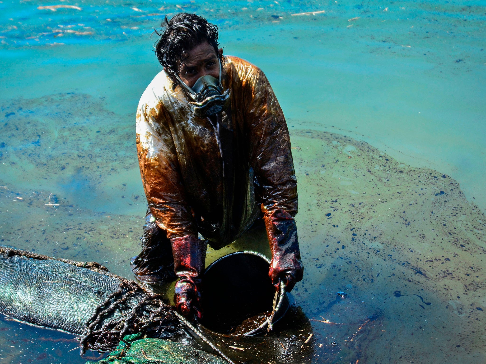 A man scoops leaked oil from the vessel MV Wakashio, which ran aground off the coast of southeast Mauritius in August