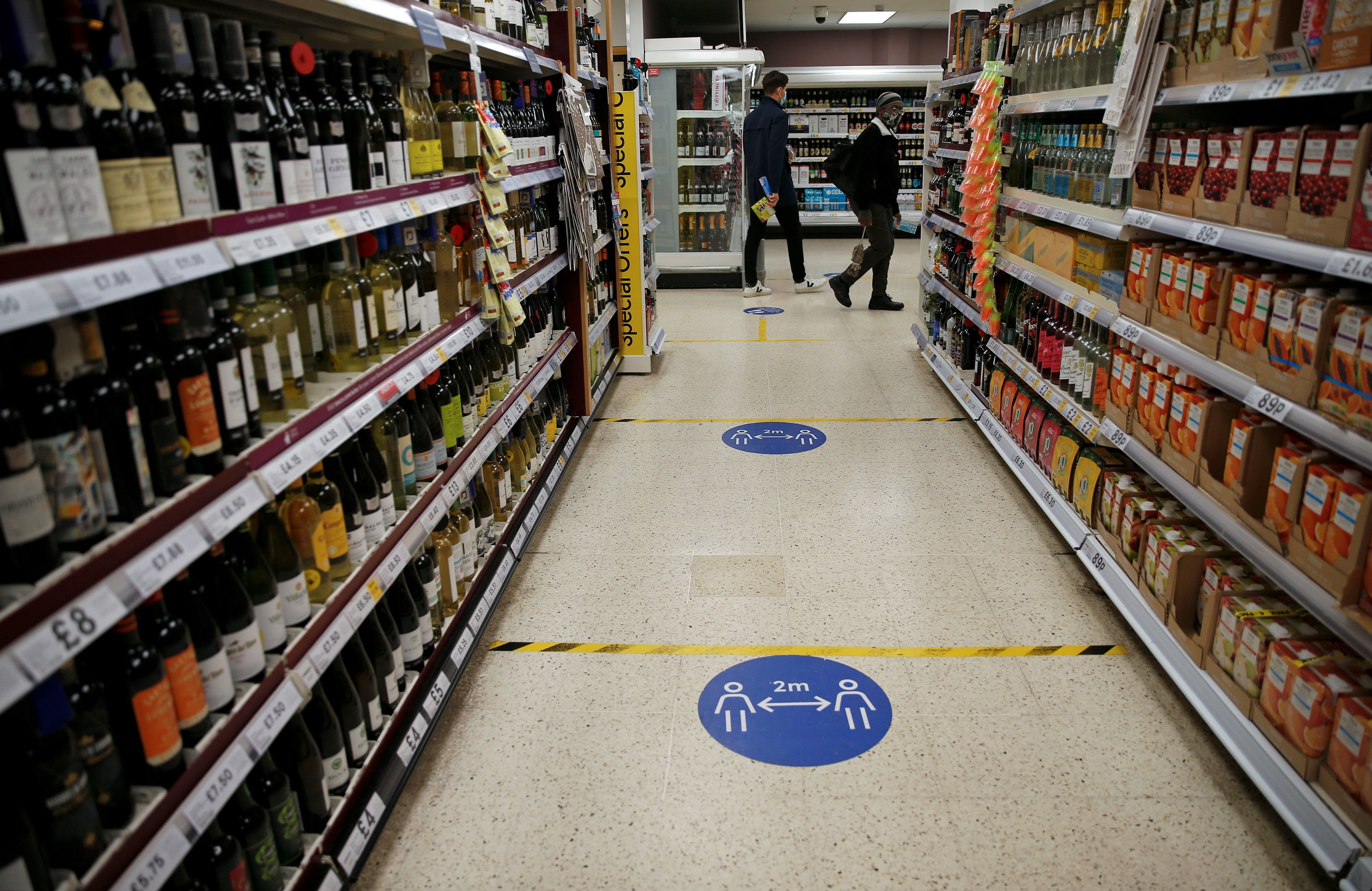 Floor stickers in the alcohol aisle inside a Tesco Metro supermarket ask customers to social distance as they shop