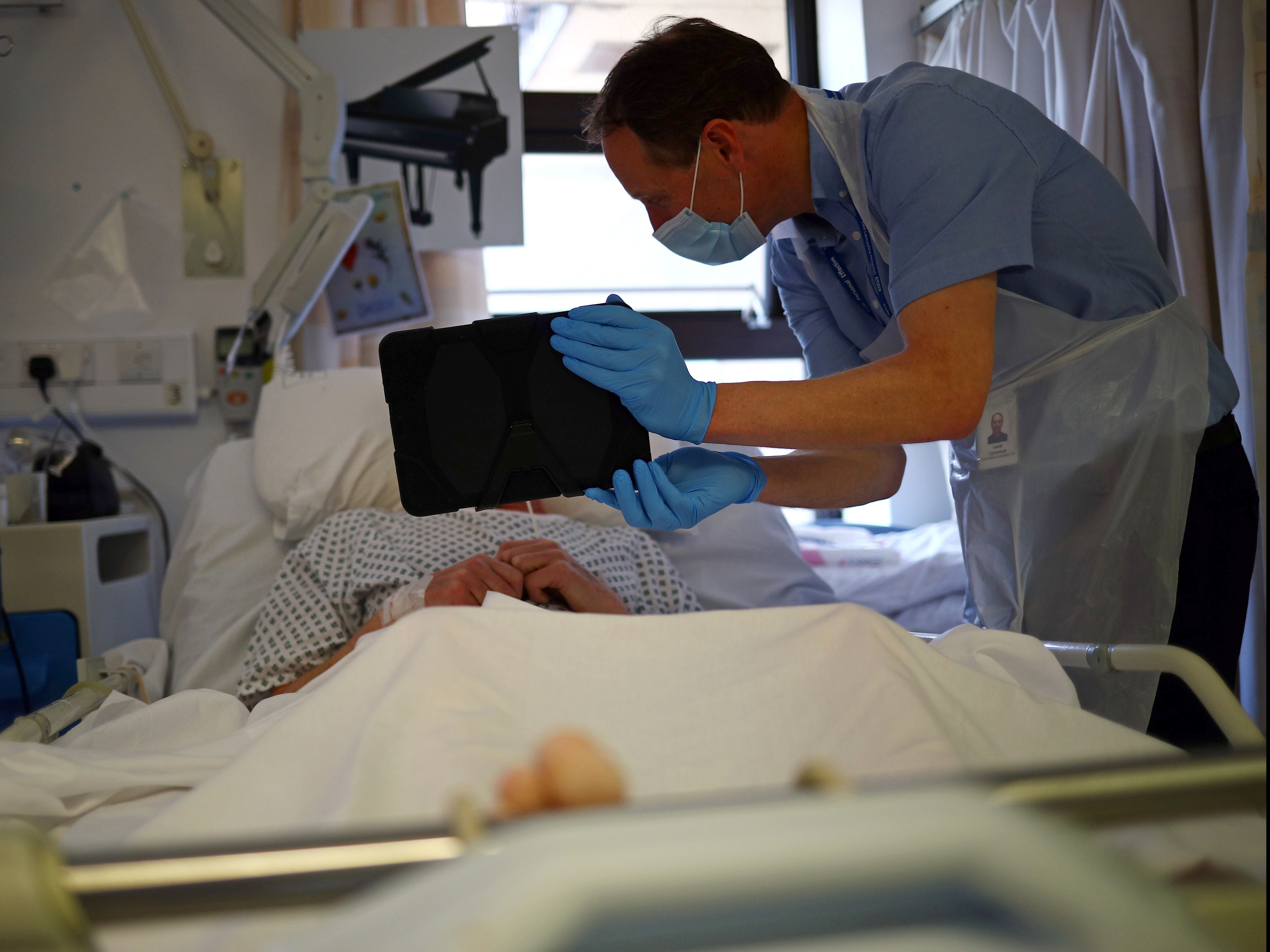 A patient communicates with family on an iPad held by a member of NHS staff