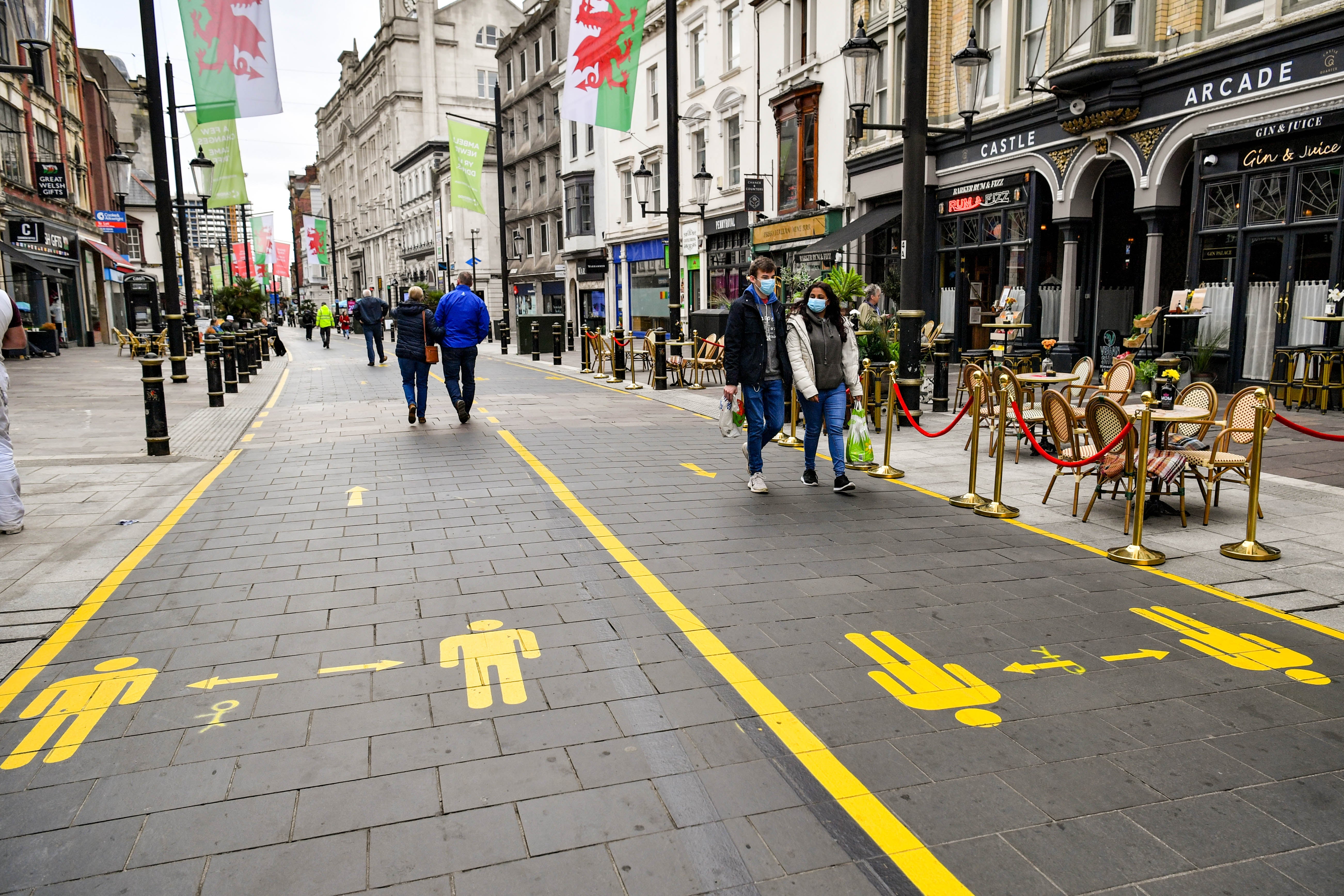 People wear face coverings as they walk along socially distanced floor markings in Cardiff after the Welsh Government placed three more areas of Wales into local lockdown.