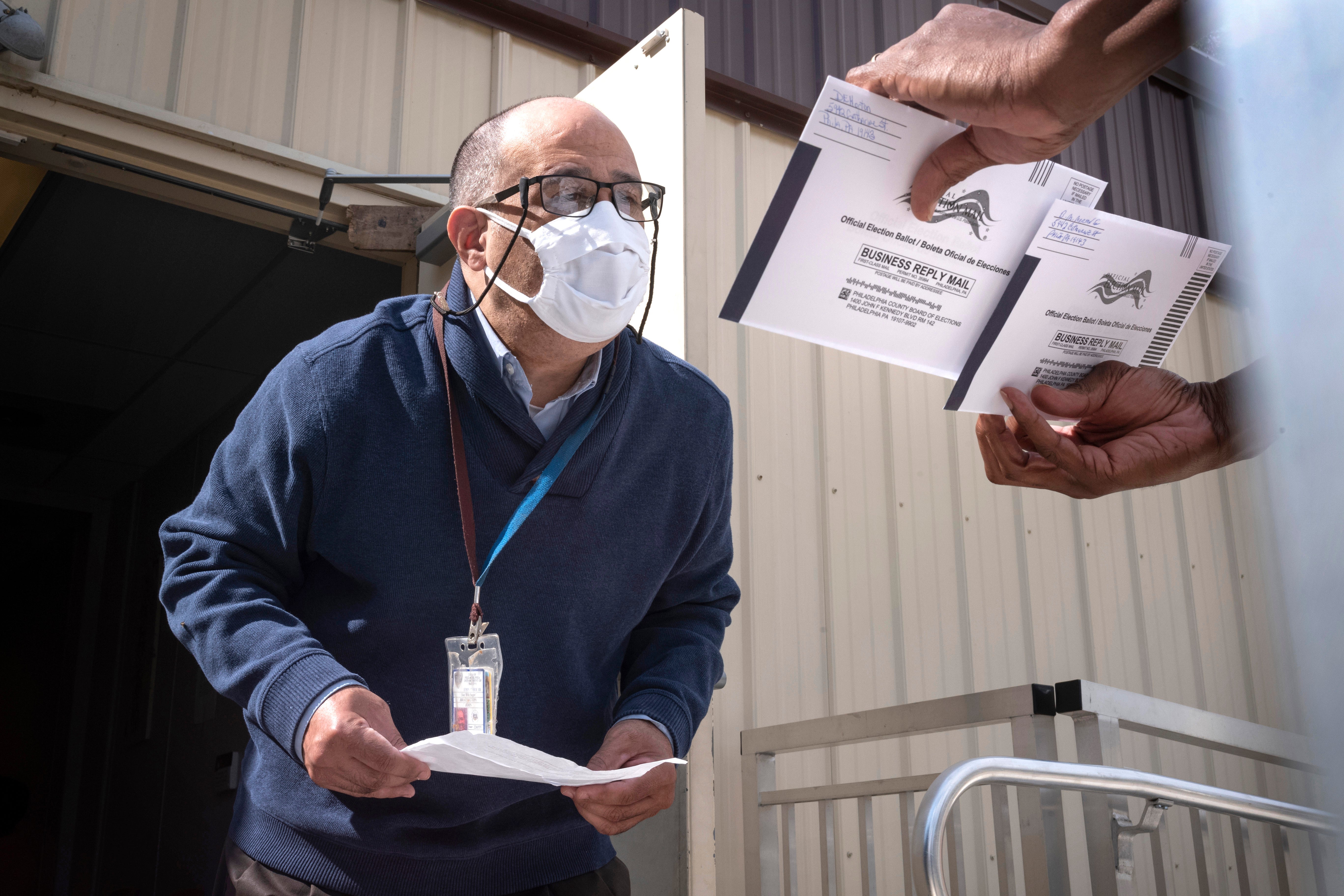 An employee of the Philadelphia Commissioners Office examines ballots at a satellite election office at Overbrook High School in Philadelphia. Local election clerks can’t start verifying mailed-in ballots in Pennsylvania until Election Day and in Michigan until the day before, which the secretary of state says is not enough time.