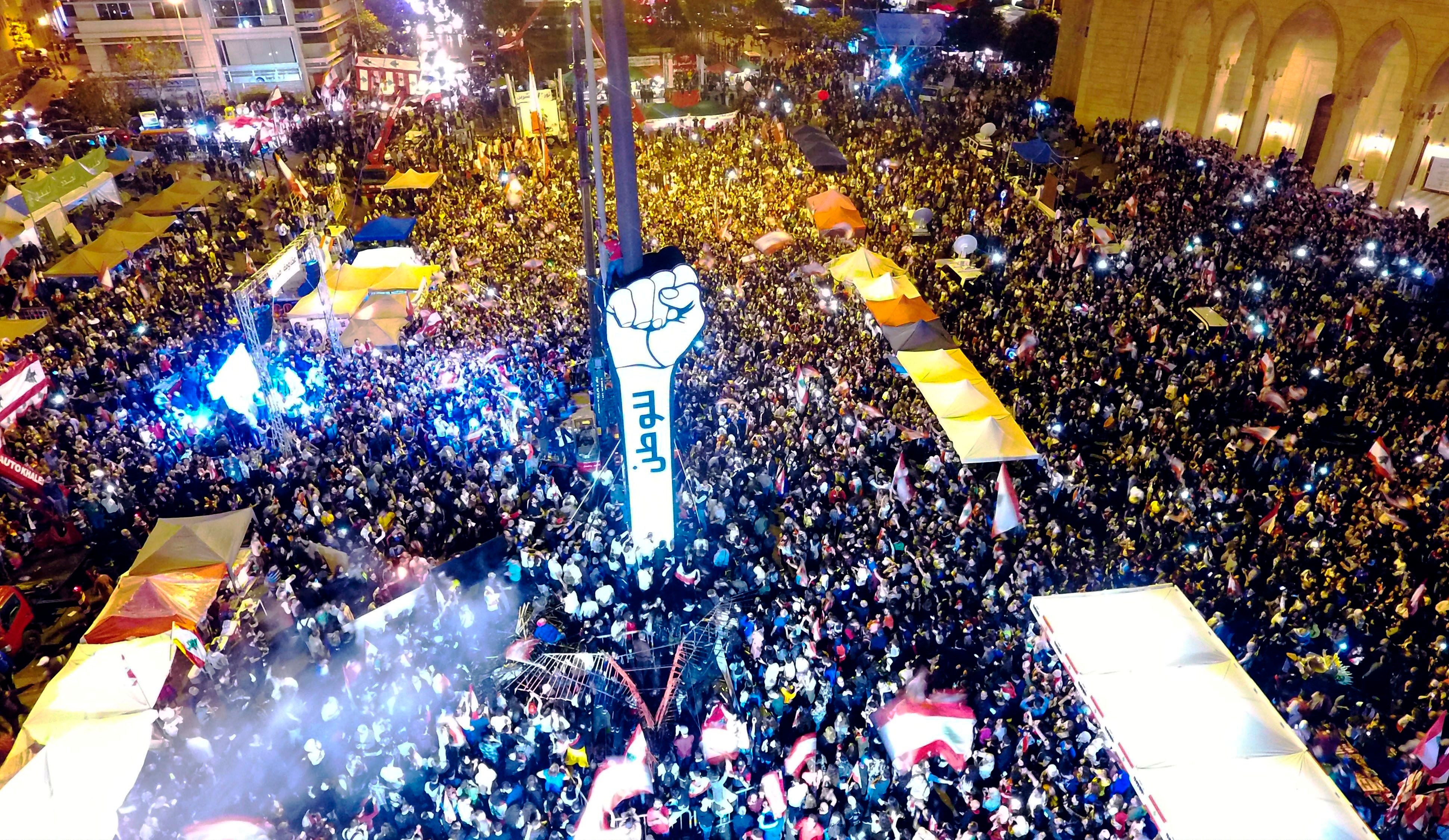 Lebanese demonstrators gather around a new giant sign of a fist that bears the Arabic word "revolution" on it Beirut's Martyr's Square