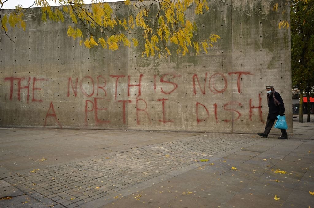 A man wearing a face-mask walks past graffiti declaring that 'the north is not a petri dish' after Greater Manchester mayor Andy Burnham threatened legal action if Tier 3 restrictions are imposed on the city without agreement