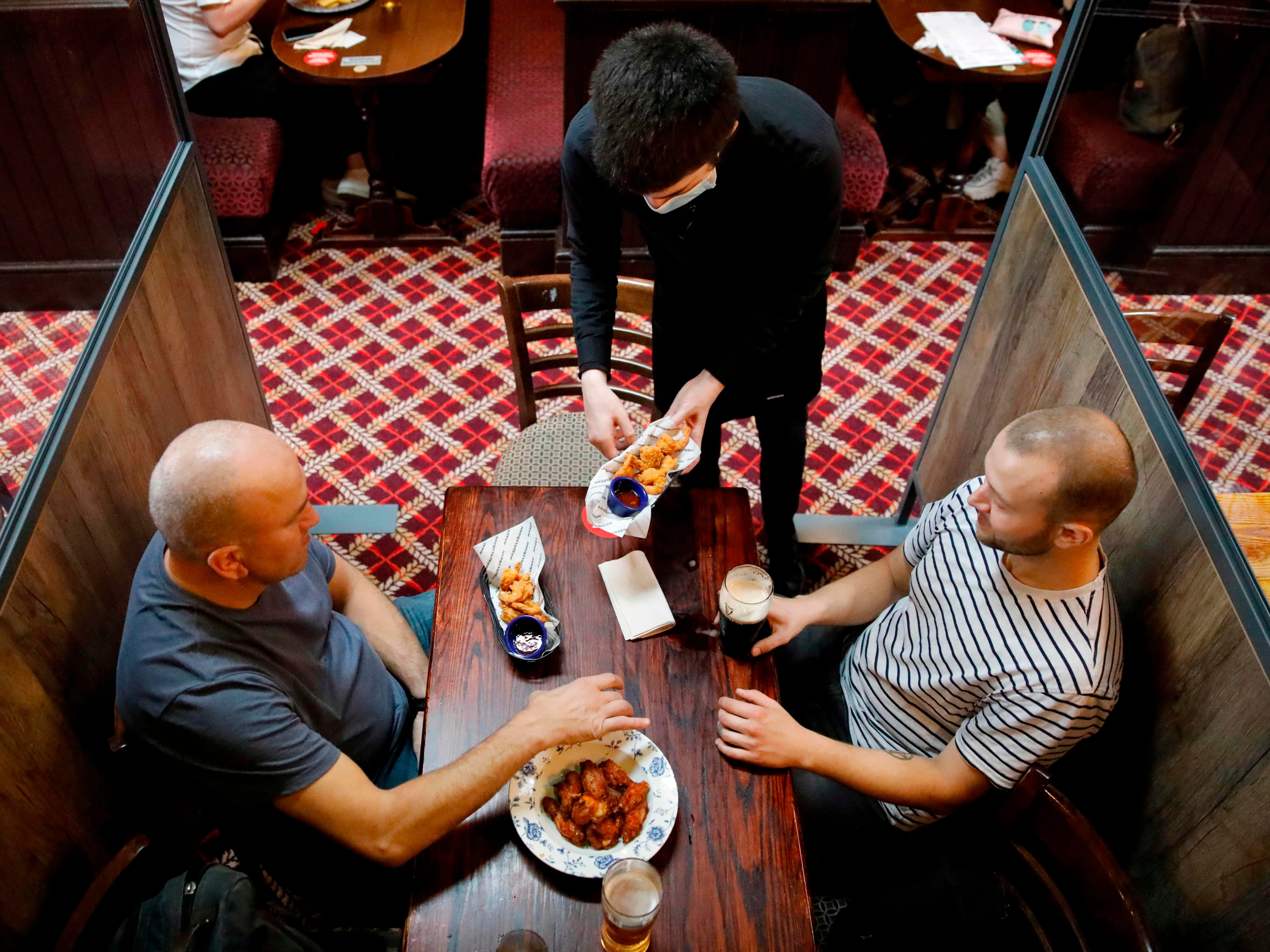 A member of bar staff wearing PPE (personal protective equipment) in the form of a face mask, serves food to seated customers inside the Wetherspoon pub