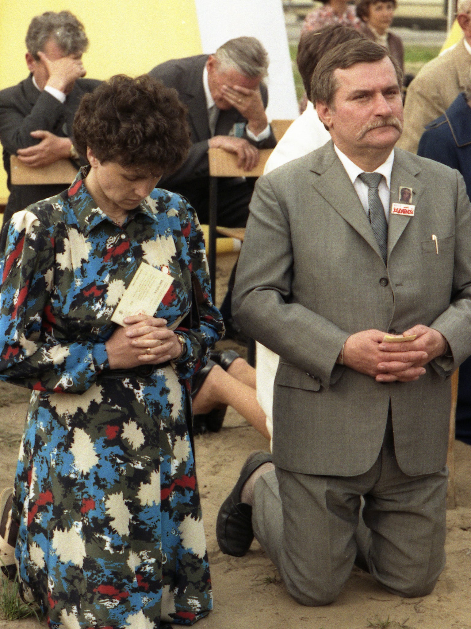 Wałęsa and his wife Danuta kneel on the ground during an open mass held by Pope John Paul II in 1987