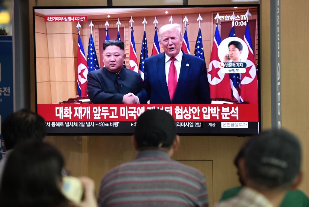 People watch a television news showing a file footage of a meeting between US President Donald Trump and North Korean leader Kim Jong Un