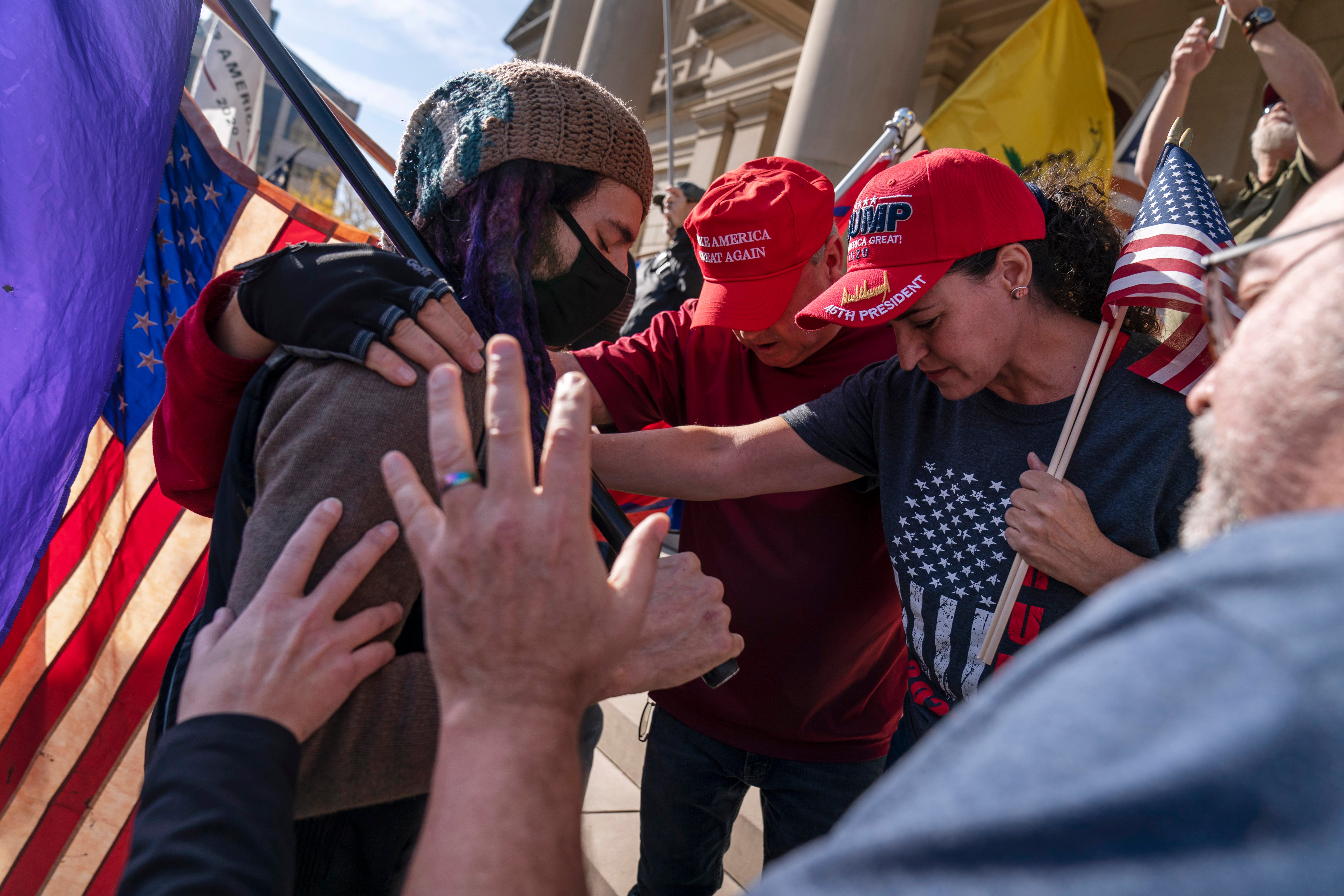 Trump supporters demonstrating during the election results, at right, pray with a counter protester after the presidential election was called for Joe Biden outside the State Capitol in Lansing, Michigan