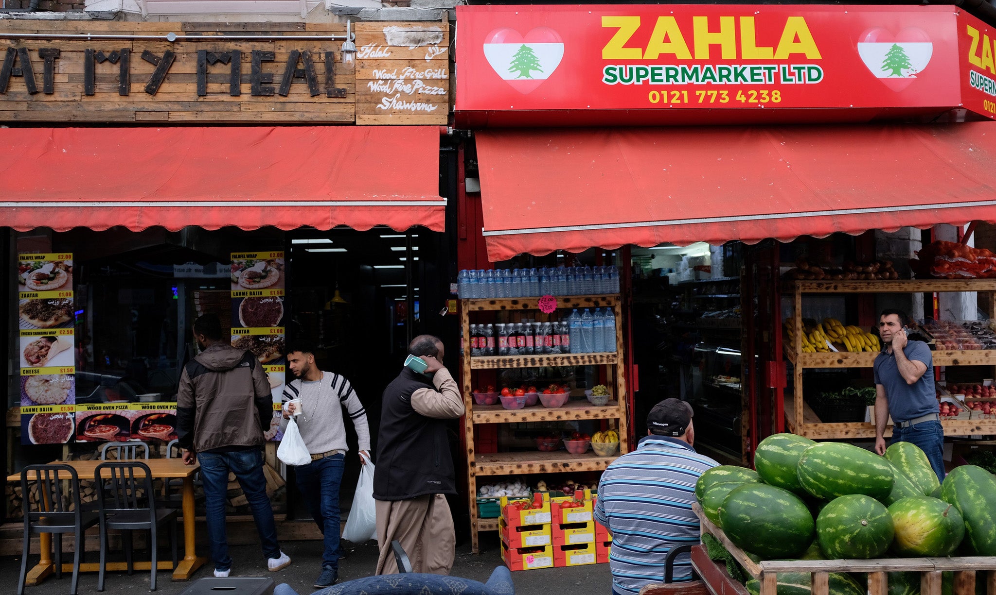 People pass a row of shops in the Sparkbrook area of Birmingham, central England, on August 15, 2018.