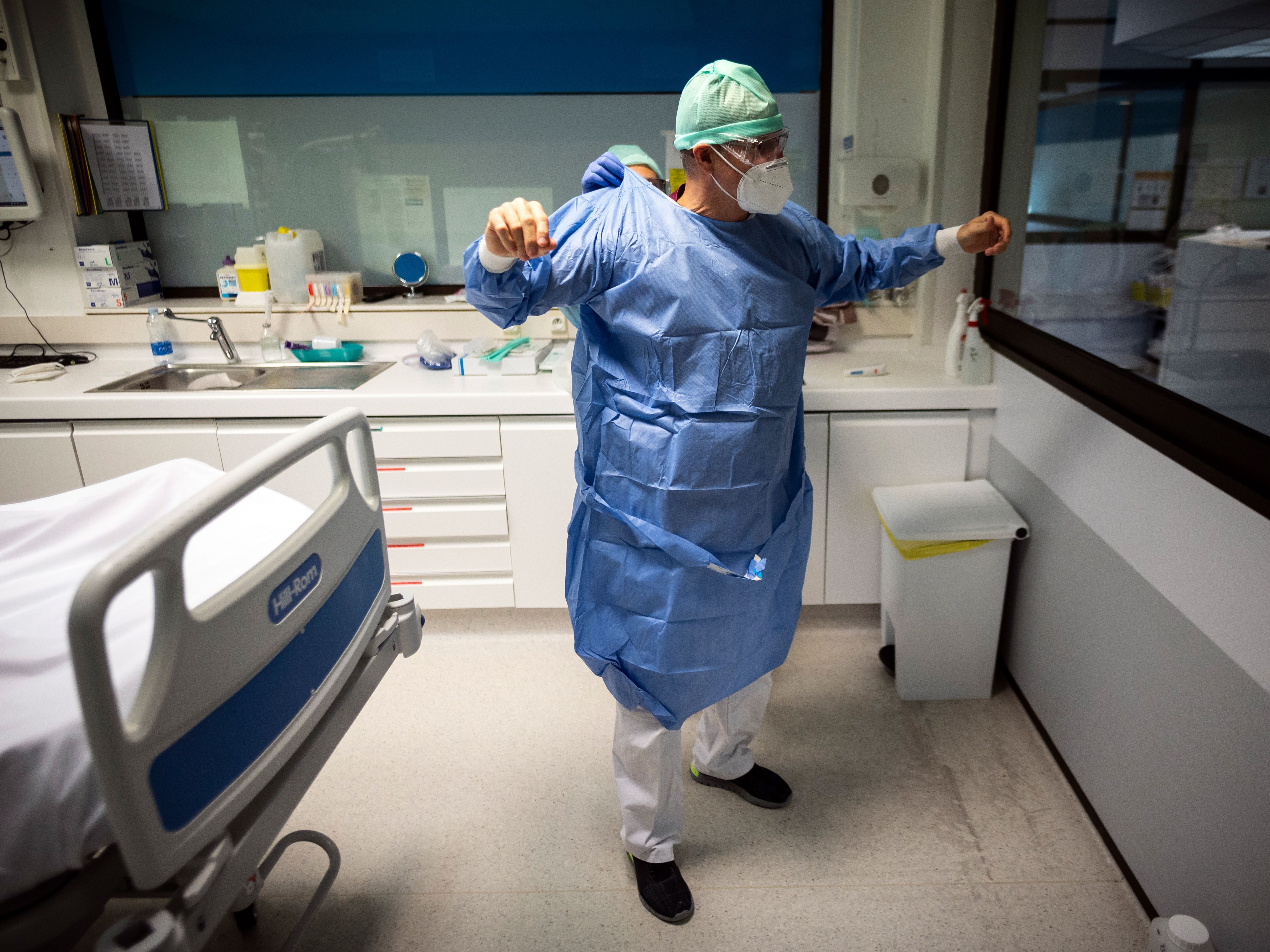 File: A nurse helps a doctor to put on his protective gear