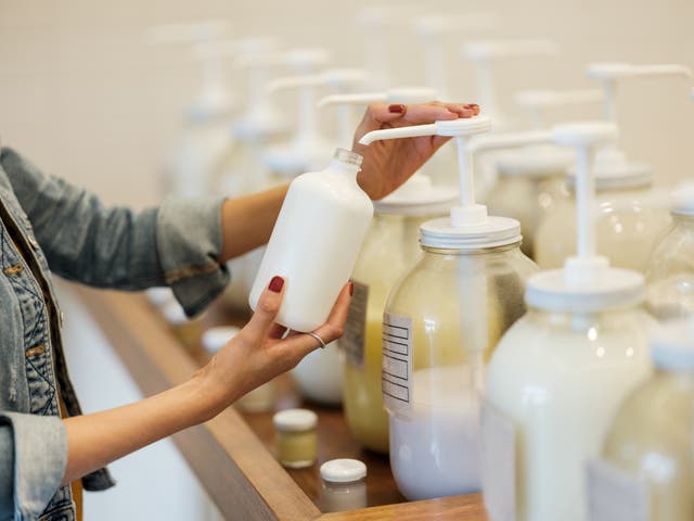 <p>A woman holding and filling up glass container with lotion at the zero waste store.&nbsp;</p>