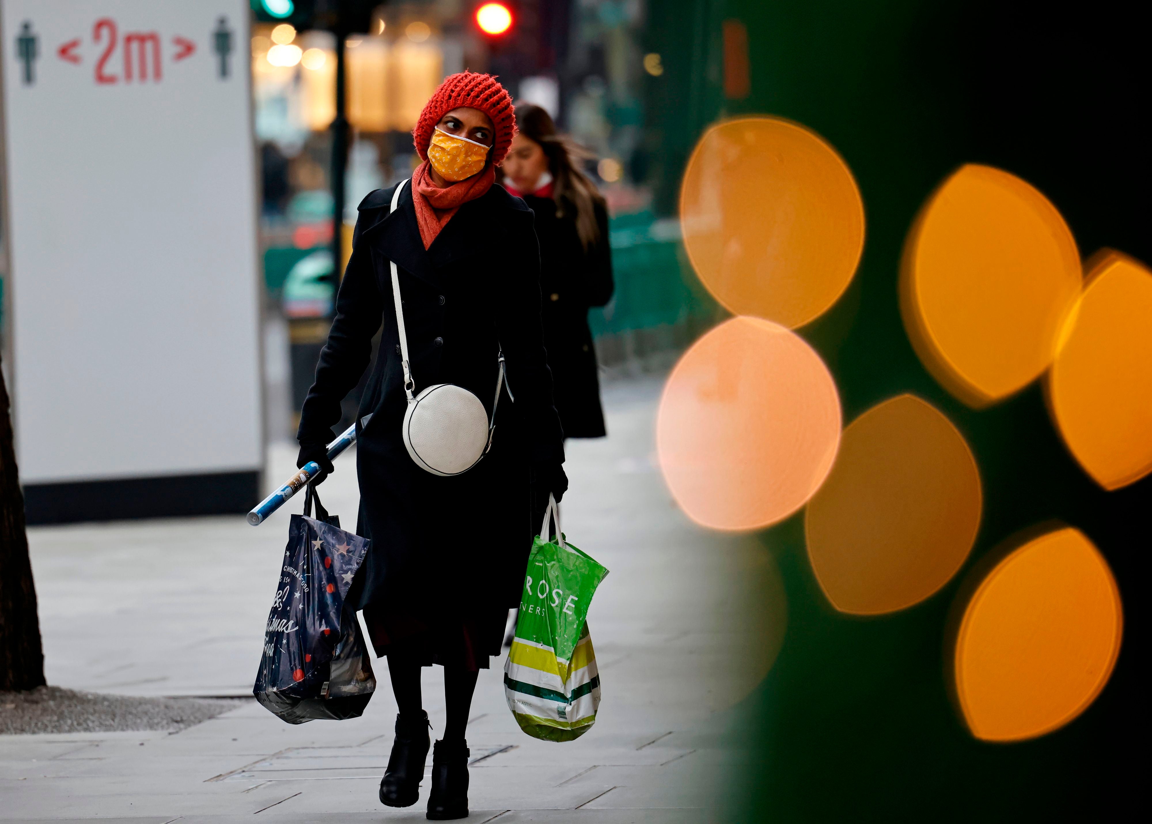 A pedestrian wearing a face mask or covering due to the COVID-19 pandemic, carries shopping bags and Christmas wrapping paper as they walk along Oxford Street in central London on 22 December, 2020.