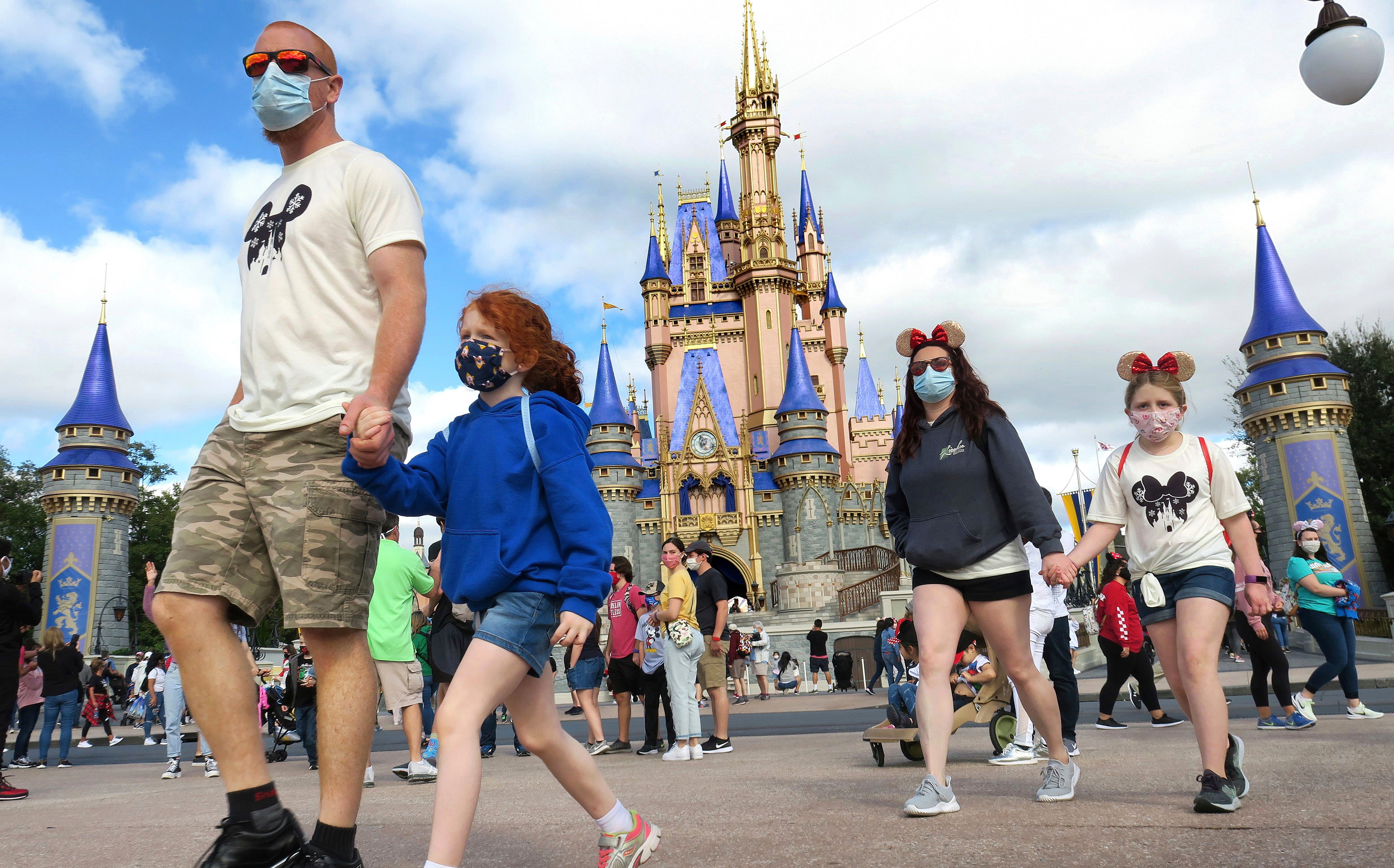 A masked family walks past Cinderella Castle in the Magic Kingdom, at Walt Disney World in Lake Buena Vista, Fla., Monday, Dec. 21, 2020. Disney's Florida parks are currently operating at 35% capacity due to the Covid-19 pandemic