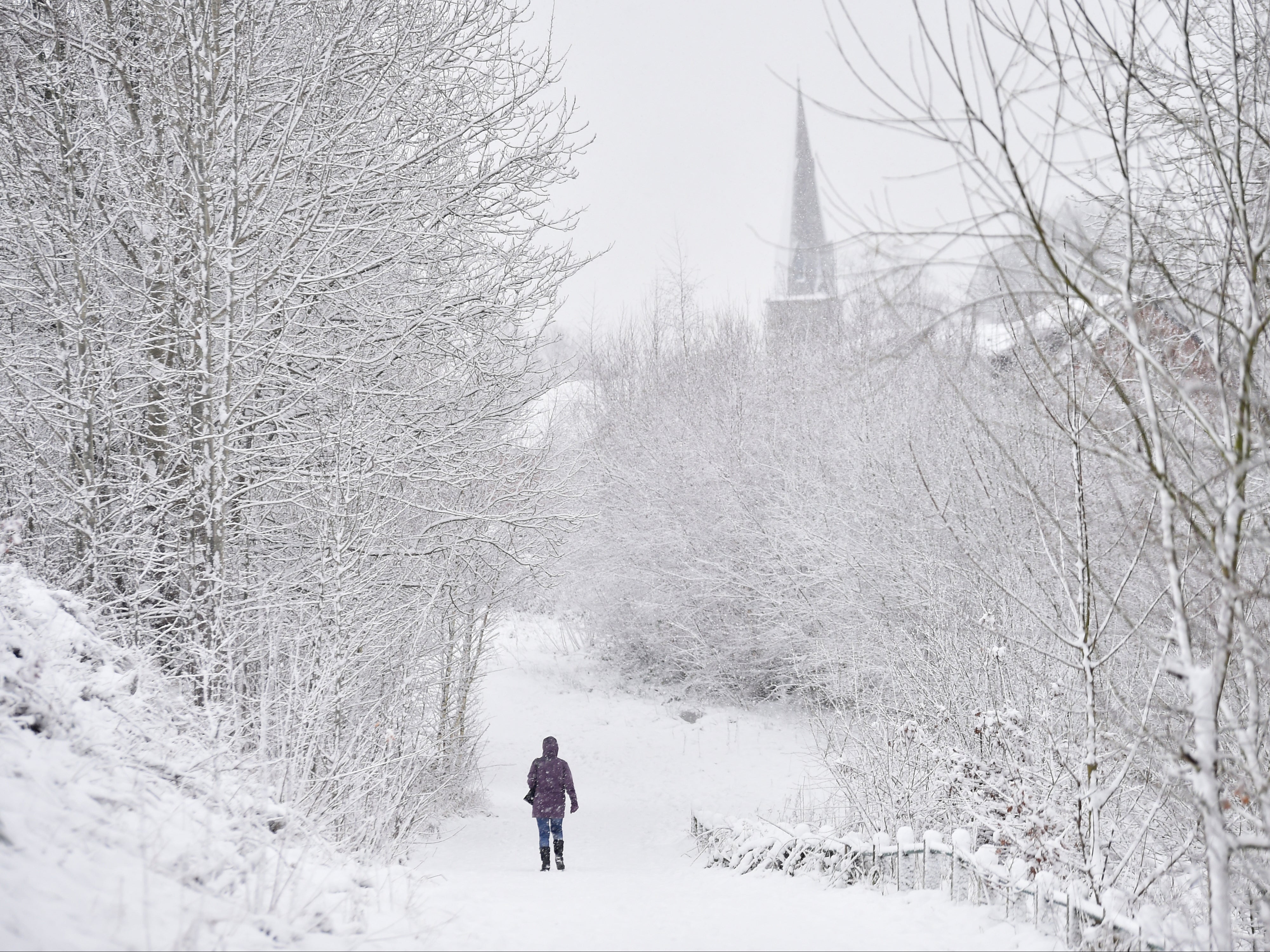 A lady walks in the snow past Silverdale Church on 29 December in Newcastle-Under-Lyme, England