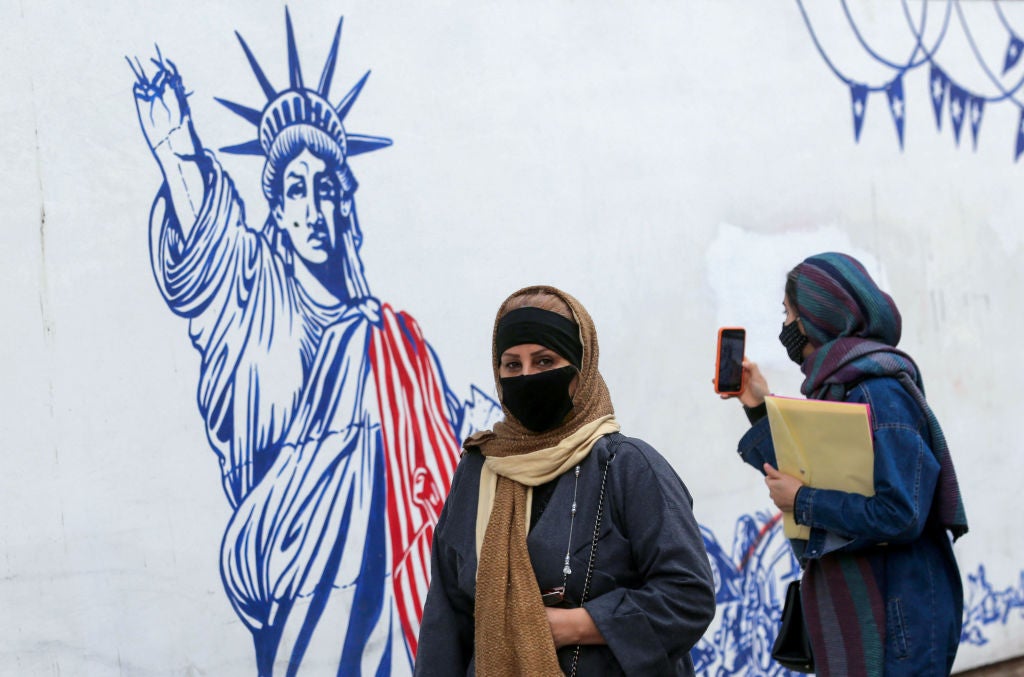 Iranian women walk past a mural painted on the outer walls of the former US embassy in the capital Tehran