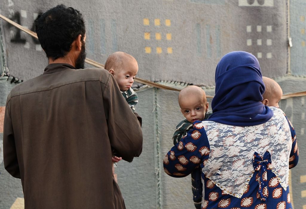 A man and woman carry malnourished children at a camp for Syrians displaced by conflict, near the town of Deir al-Ballu.