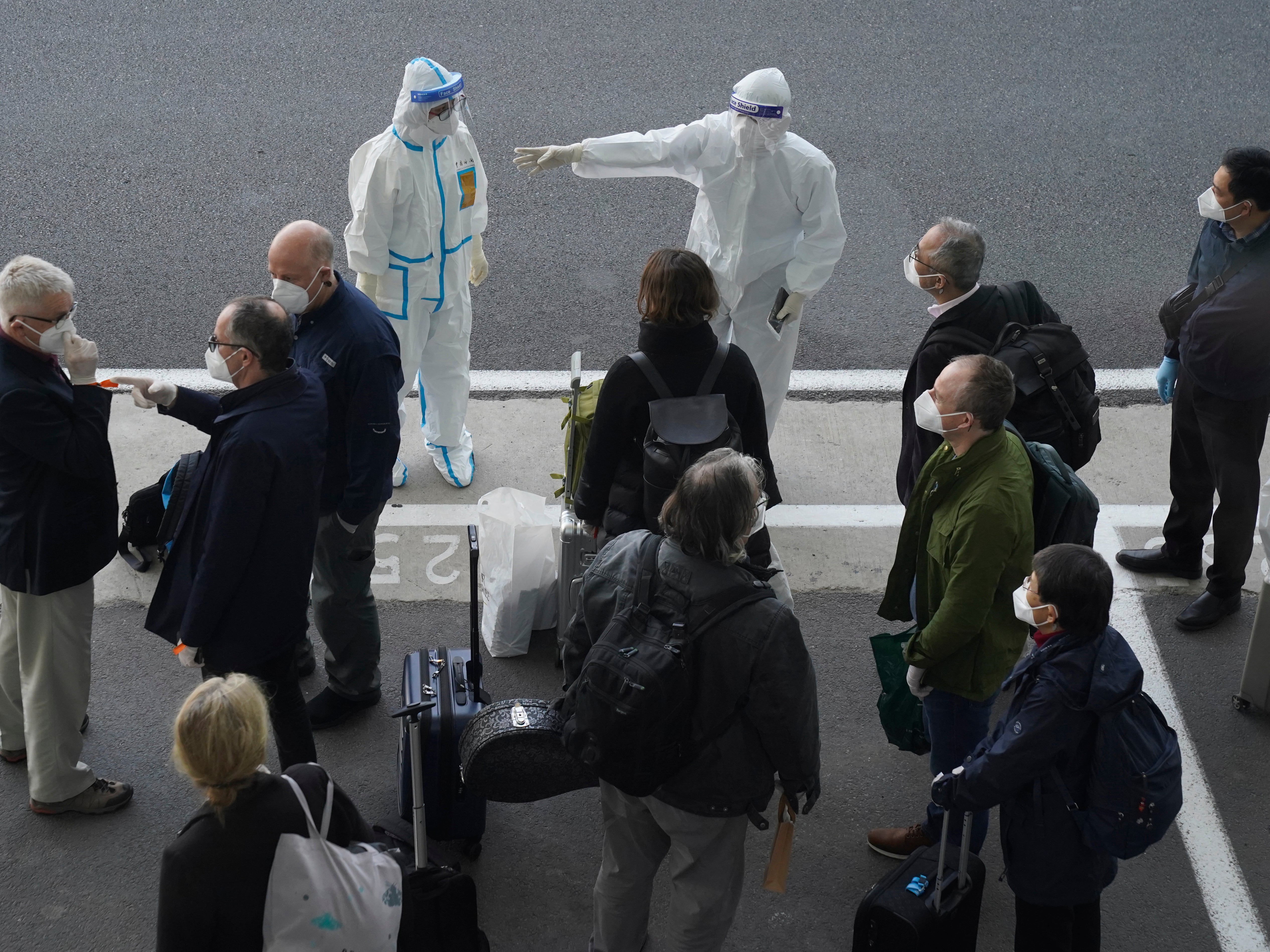 A worker in protective coverings directs members of the World Health Organization (WHO) team on their arrival at the airport in Wuhan in central China's Hubei province