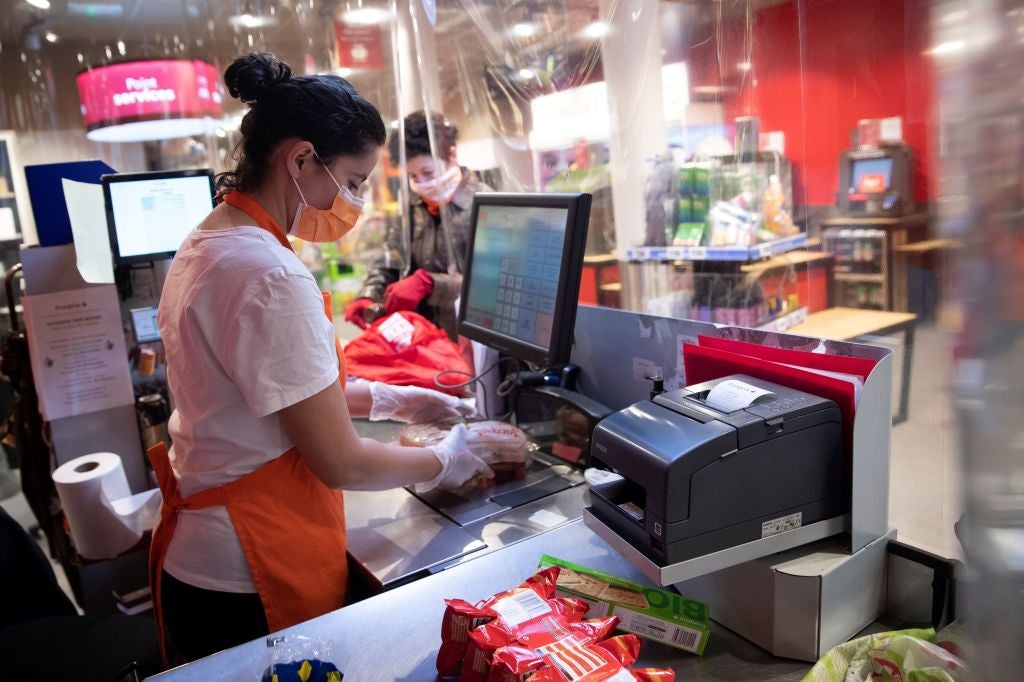 A woman works on a checkout behind a plastic screen to reduce the risk of coronavirus transmission