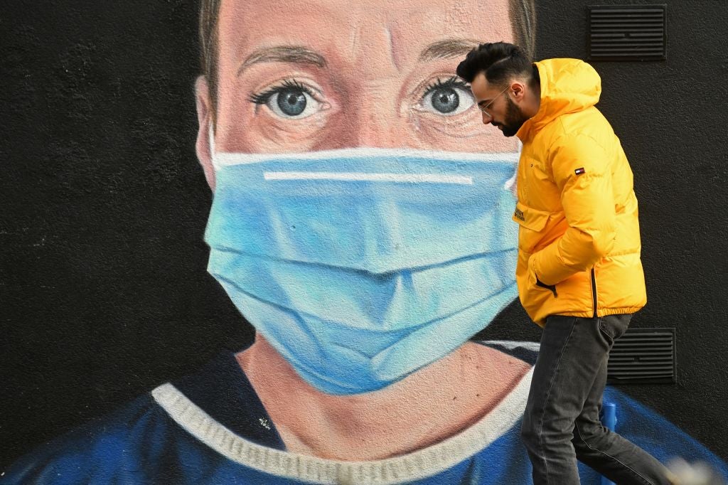 A pedestrian in Manchester walks past graffiti by the artist @akse_p19, depicting an NHS nurse in scrubs and a mask