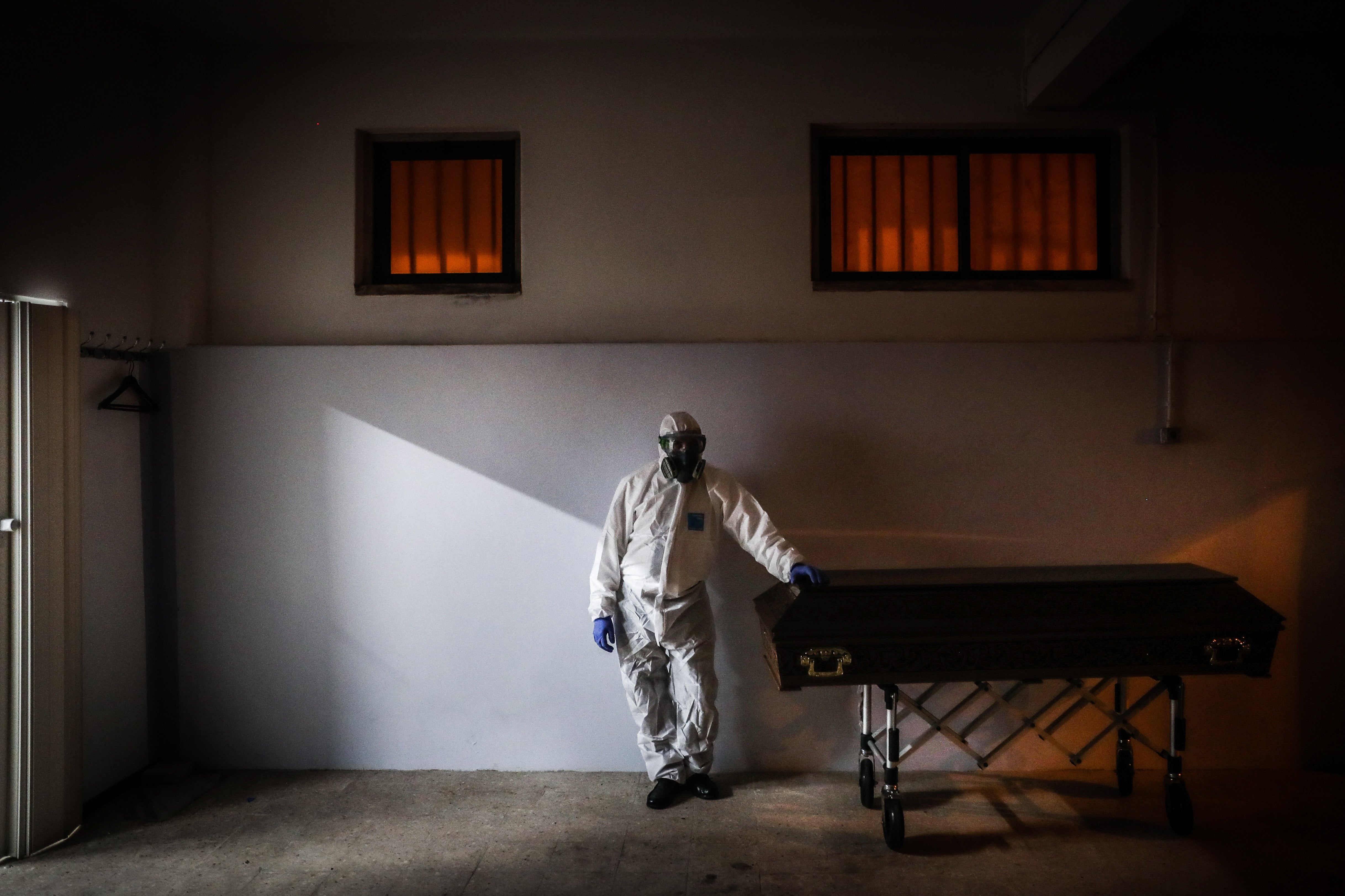 A funerary worker wears PPE next to a Covid patient’s coffin