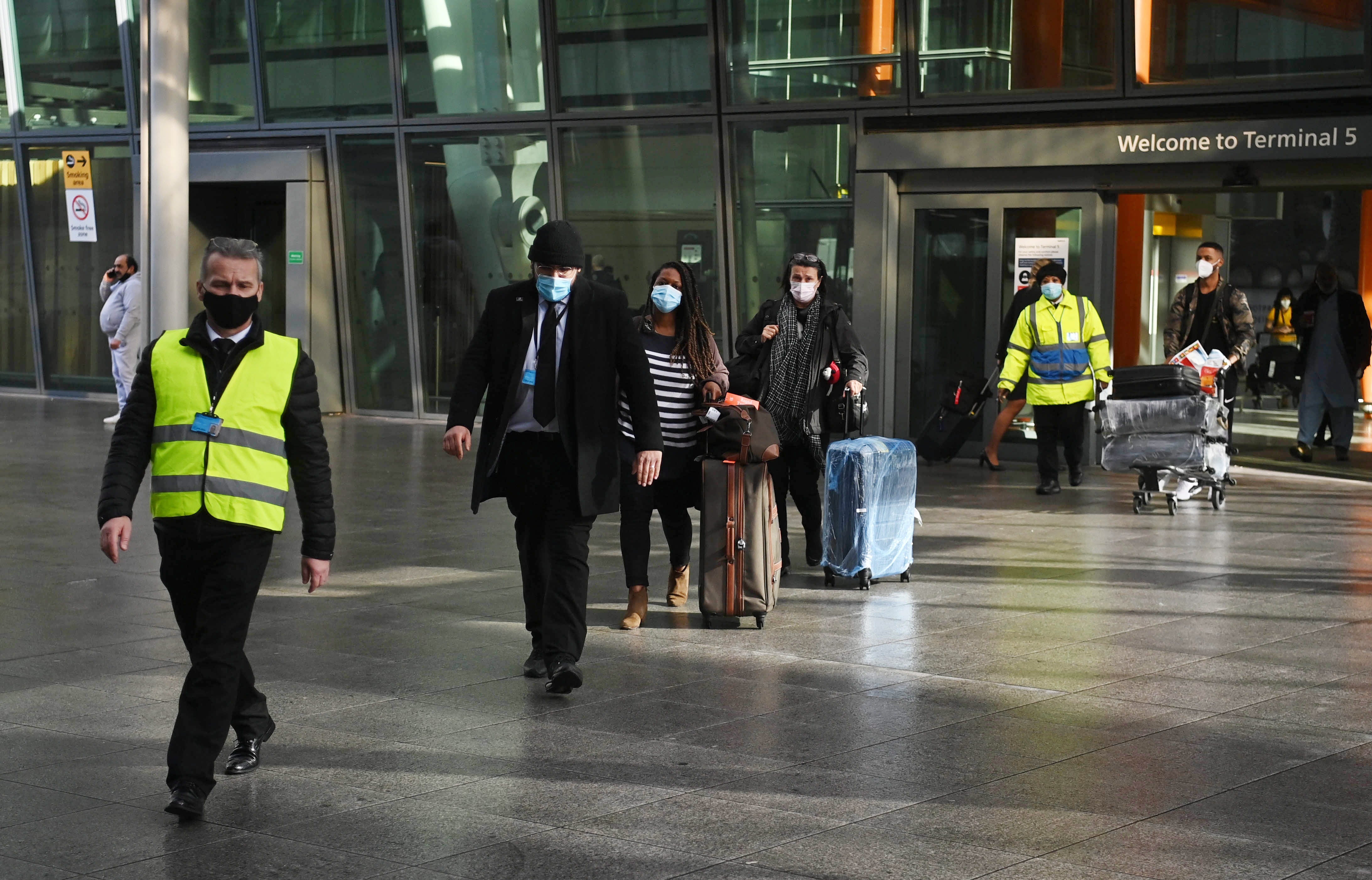 International travellers are escorted to a bus as they are moved to a Radison Blu hotel for quarantine from Heathrow airport on Monday