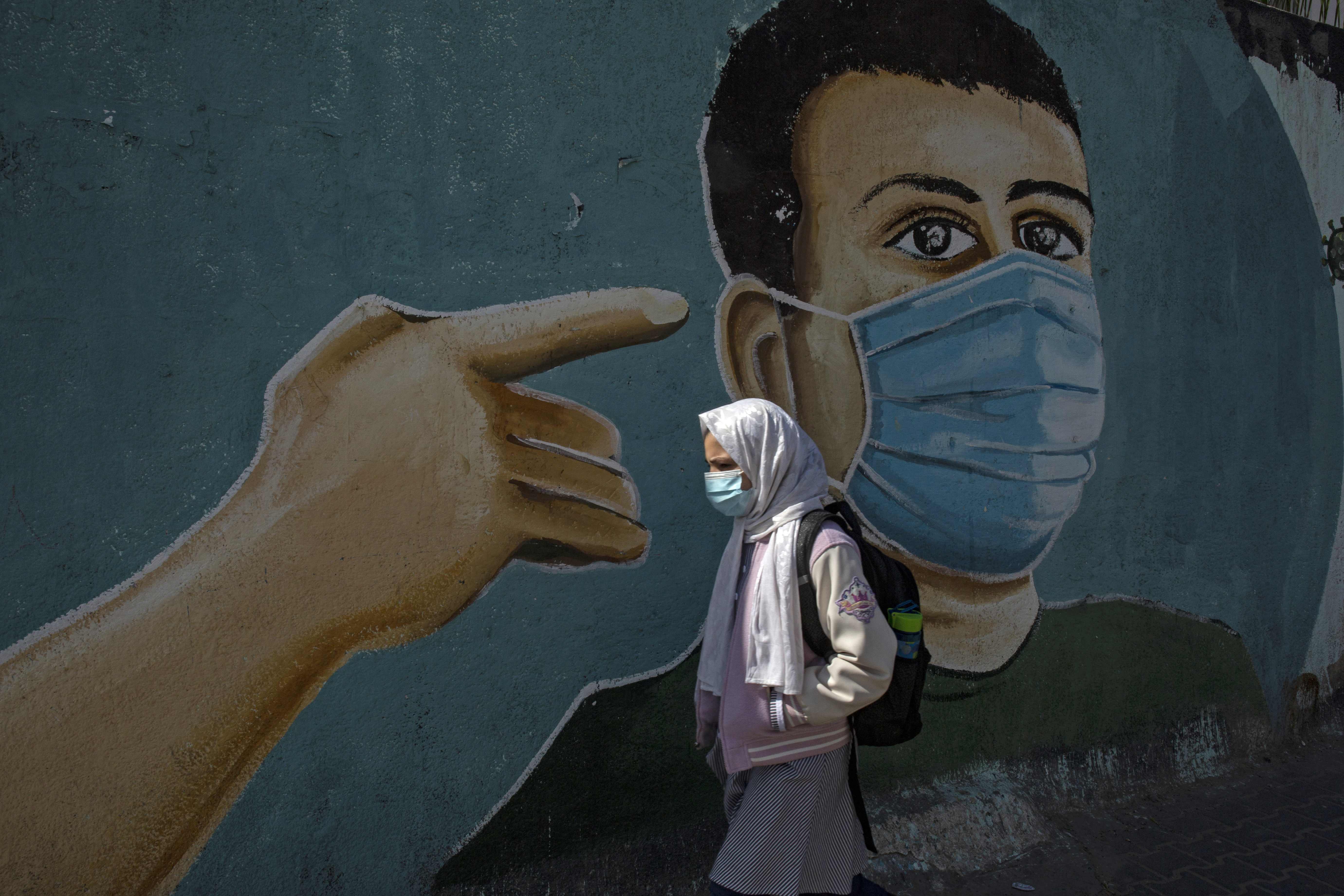 A Palestinian girl walks past a coronavirus-themed mural in Rafah in the southern Gaza Strip