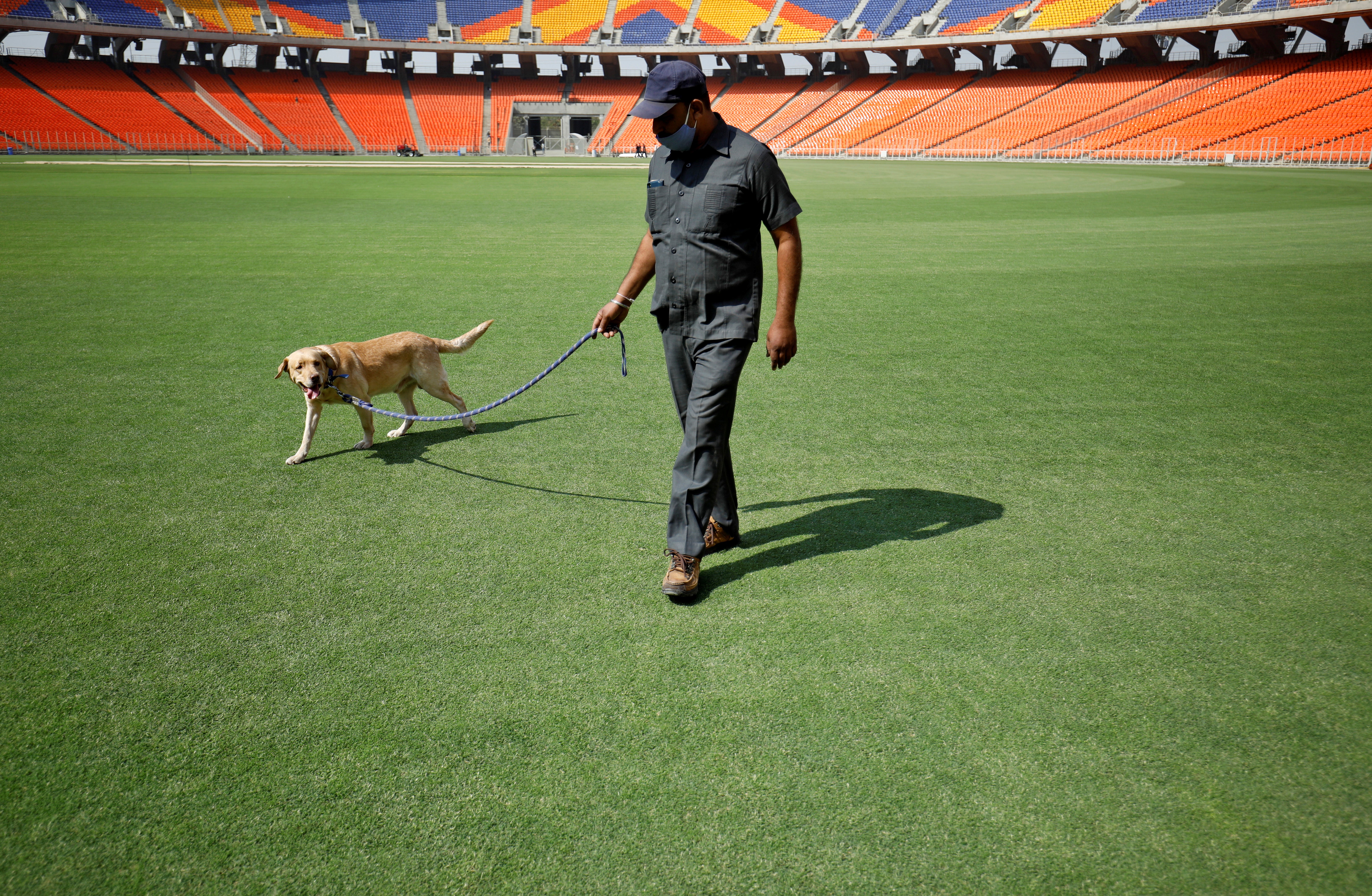 A member of a bomb disposal squad from Gujarat Police walks with a sniffer dog to scan the field at Sardar Patel Gujarat Stadium, where India and England are scheduled to play their third test match in Ahmedabad, India