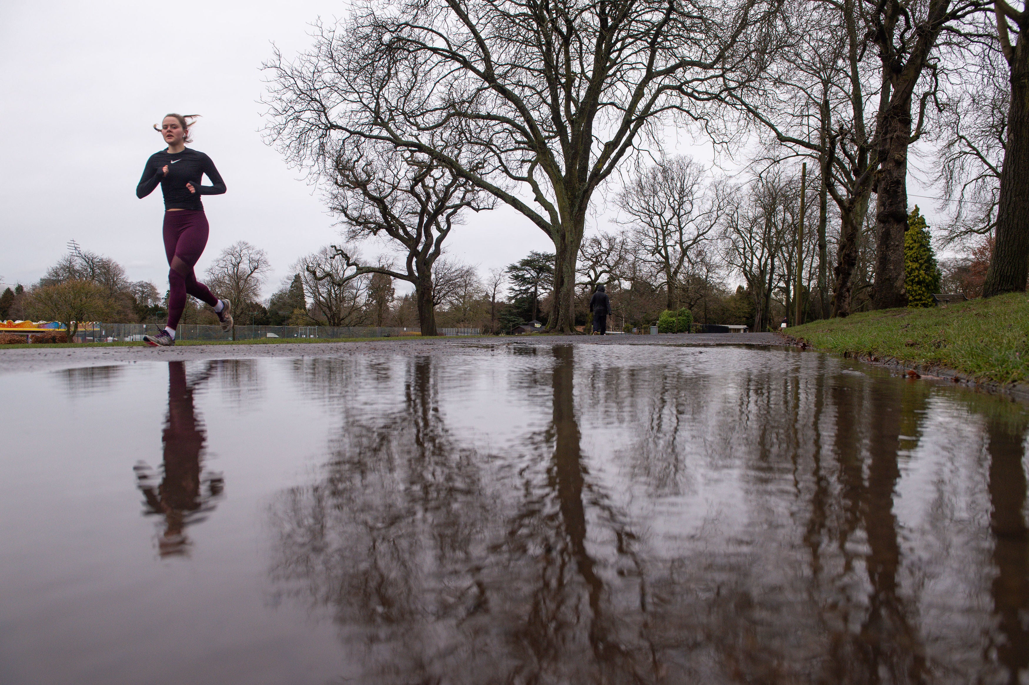 A runner is reflected in a puddle after heavy rain at Cannon Hill Park in Birmingham.