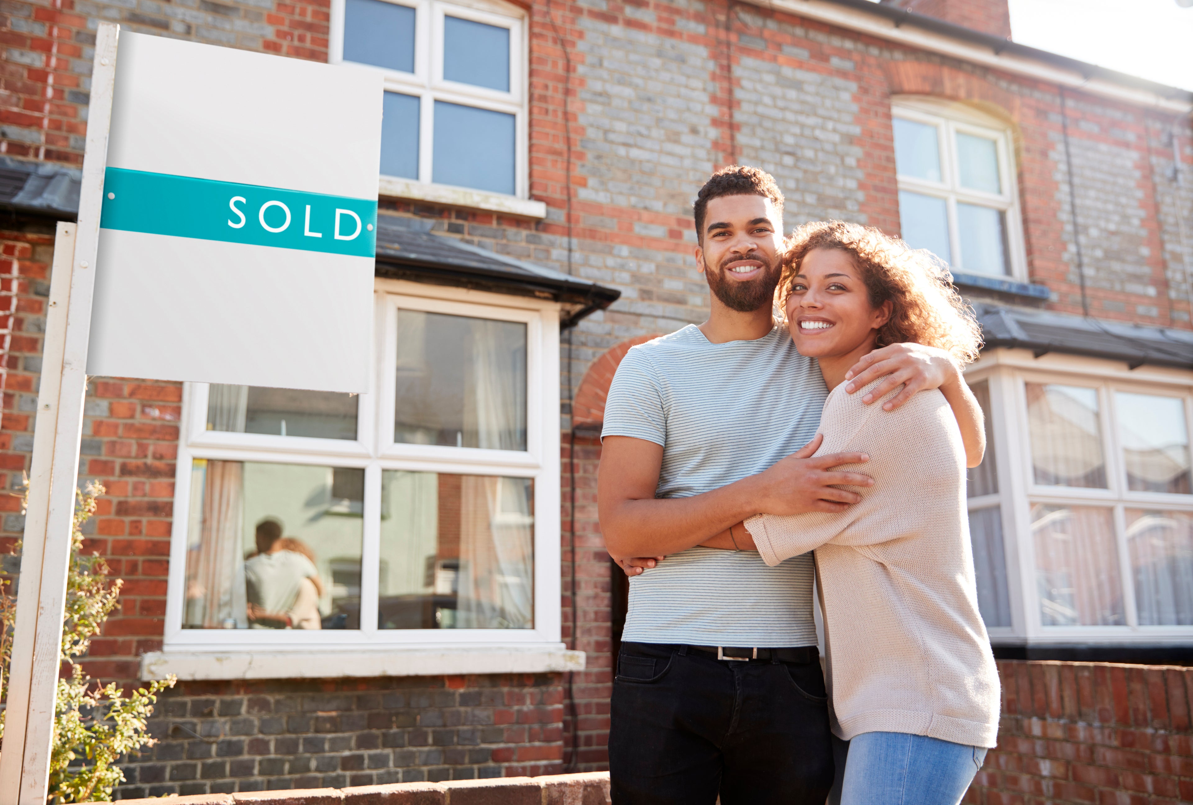 Happy couple hugging outside their new home with a 'sold' sign