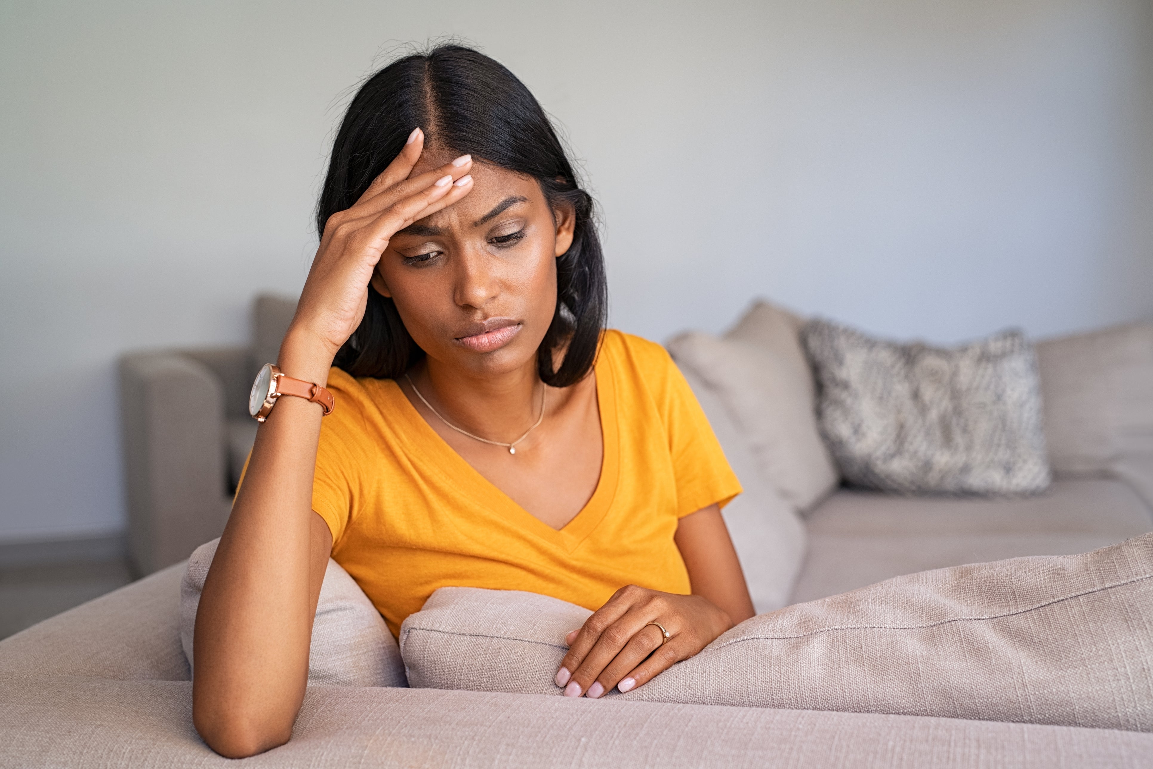 Asian woman sitting on sofa looking distressed