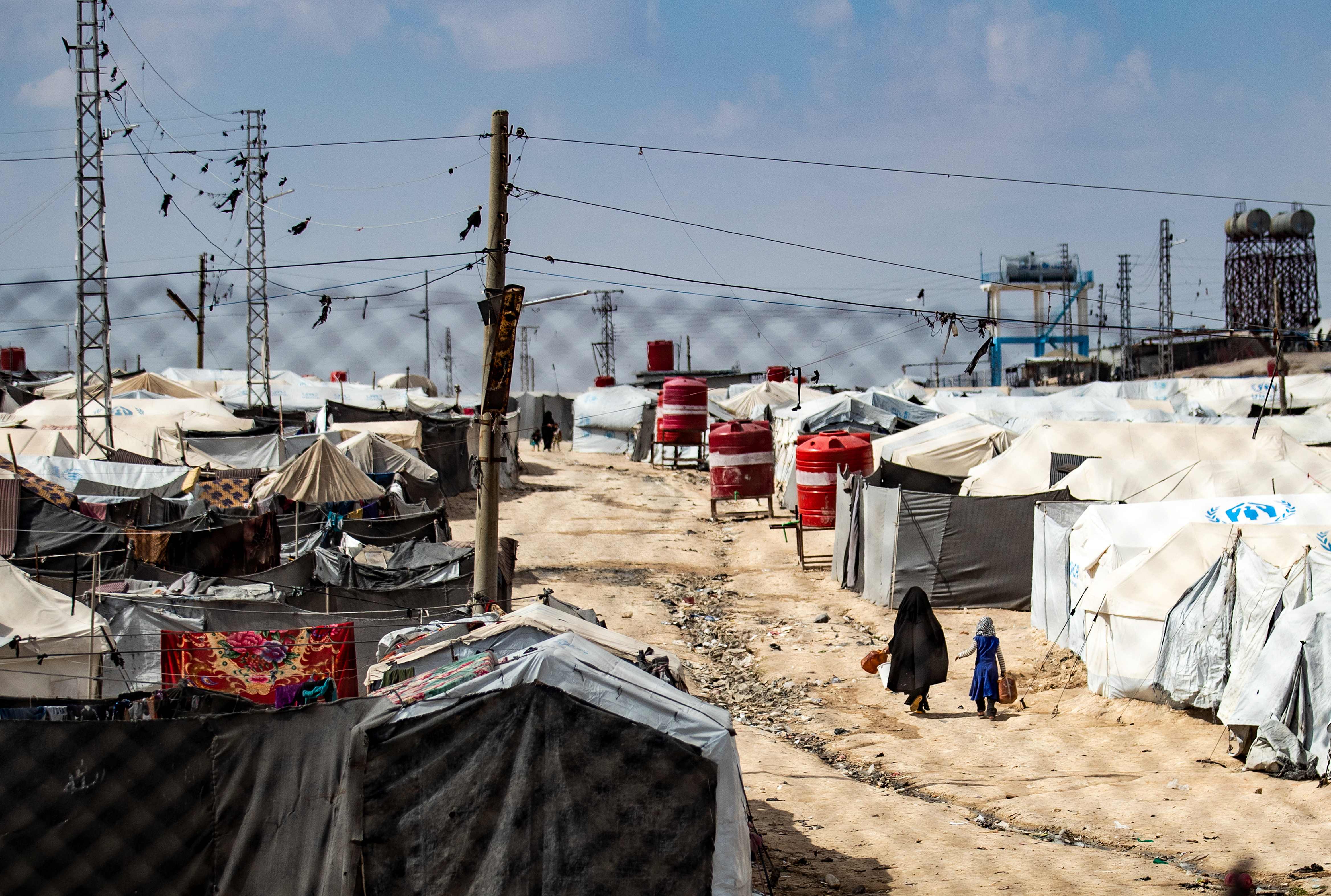 A woman and a child walk between tents at the Kurdish-run al-Hol camp