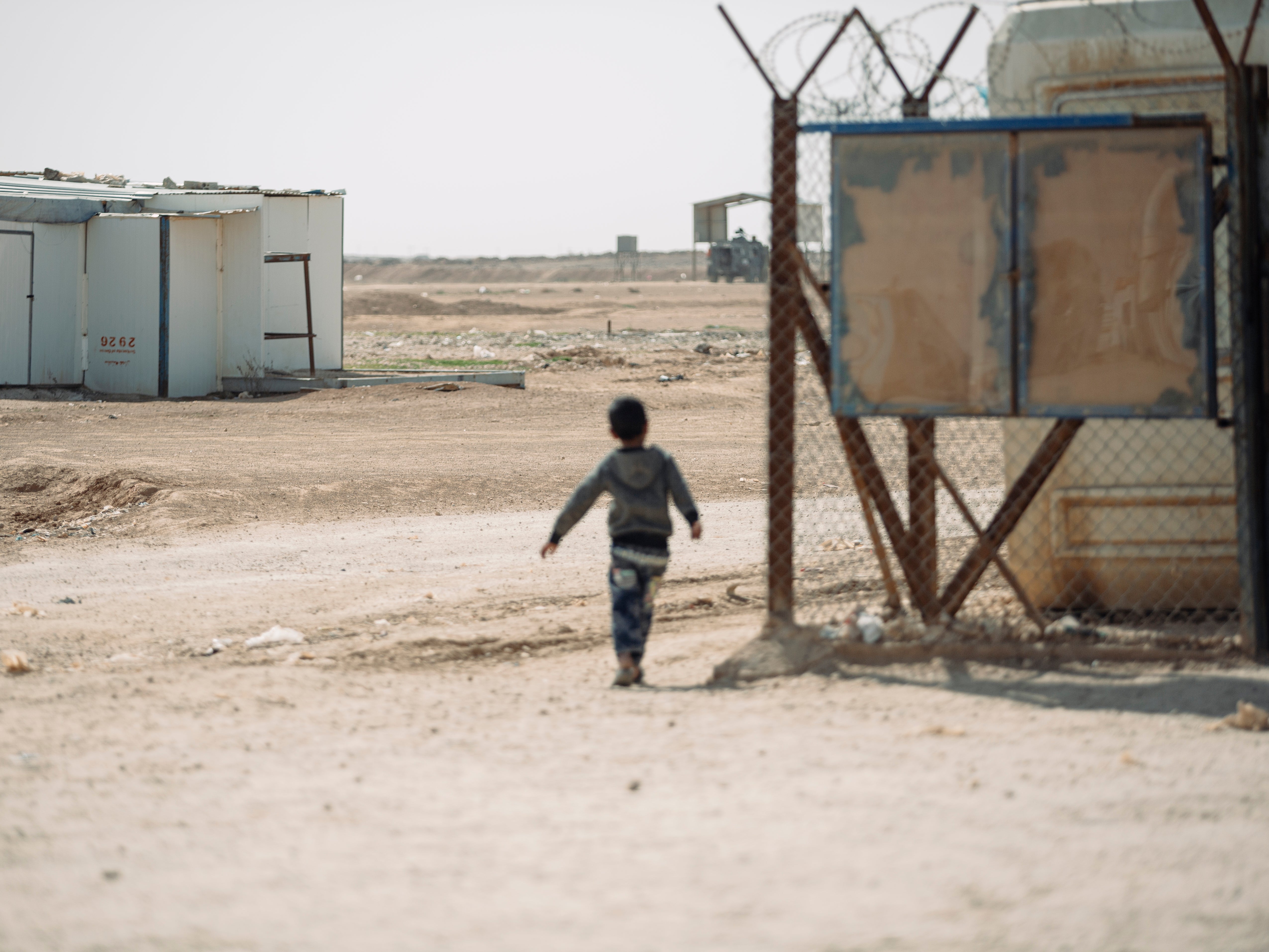 A young boy works home in Zaatari Refugee camp, Jordan. In the distance a military armoured vehicle keeps watch over the Syrian border