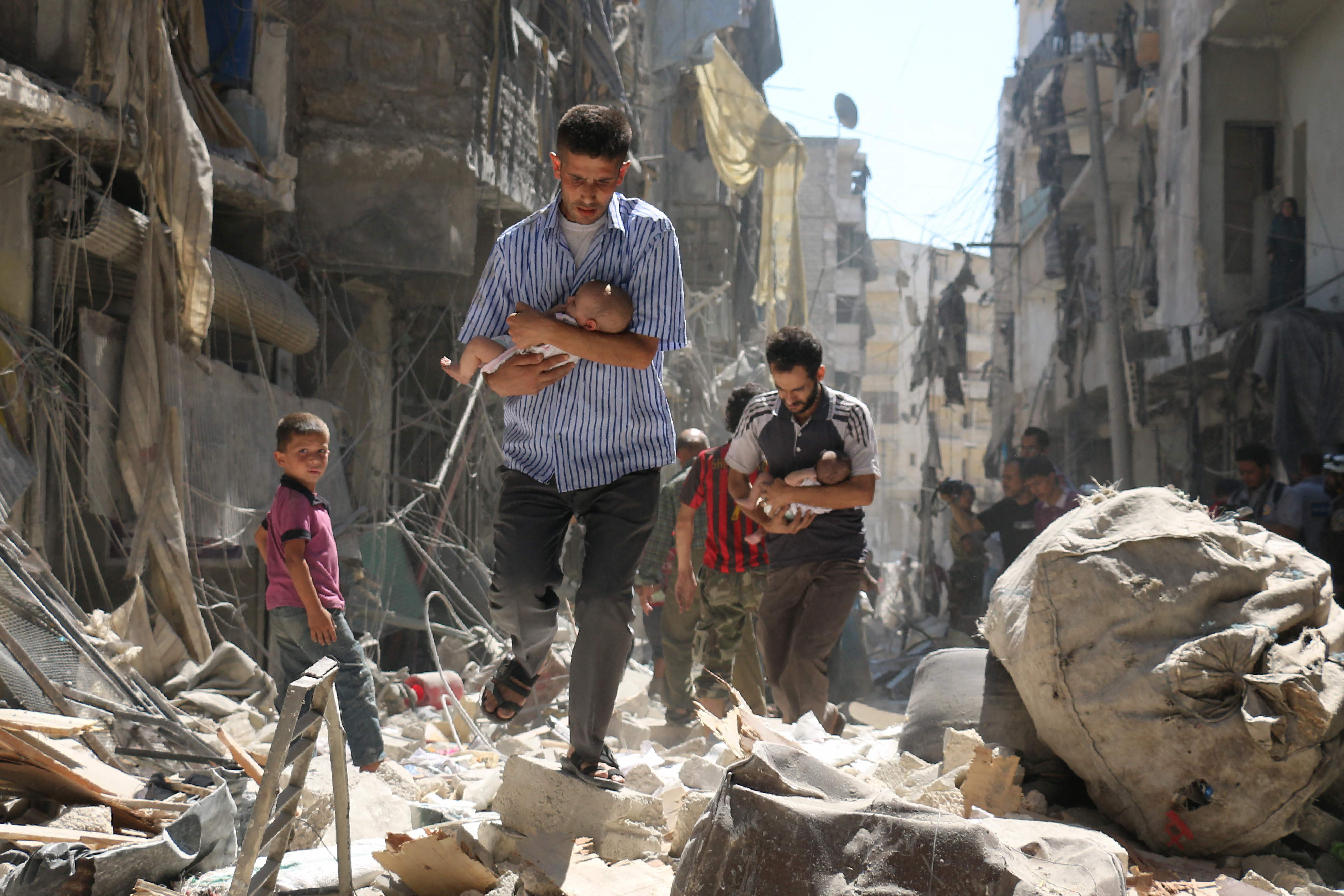 Men carrying babies make their way through the rubble of destroyed buildings in Aleppo’s rebel-held Salihin neighbourhood, in September 2016