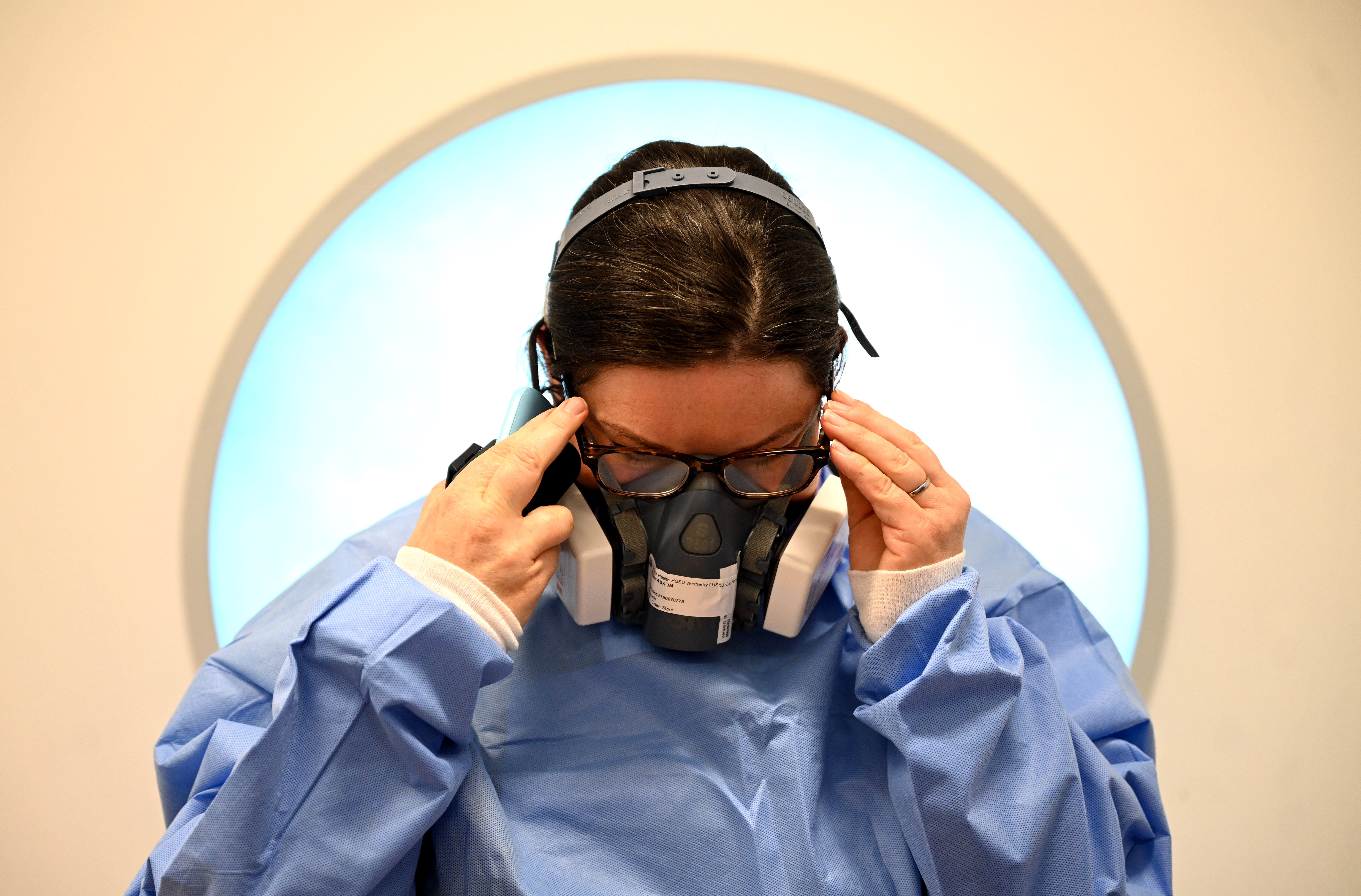 A member of the clinical staff adjusts her glasses as she dons personal protective equipment (PPE) including a mask and gown at the Intensive Care unit at Royal Papworth Hospital in Cambridge, on 5 May, 2020