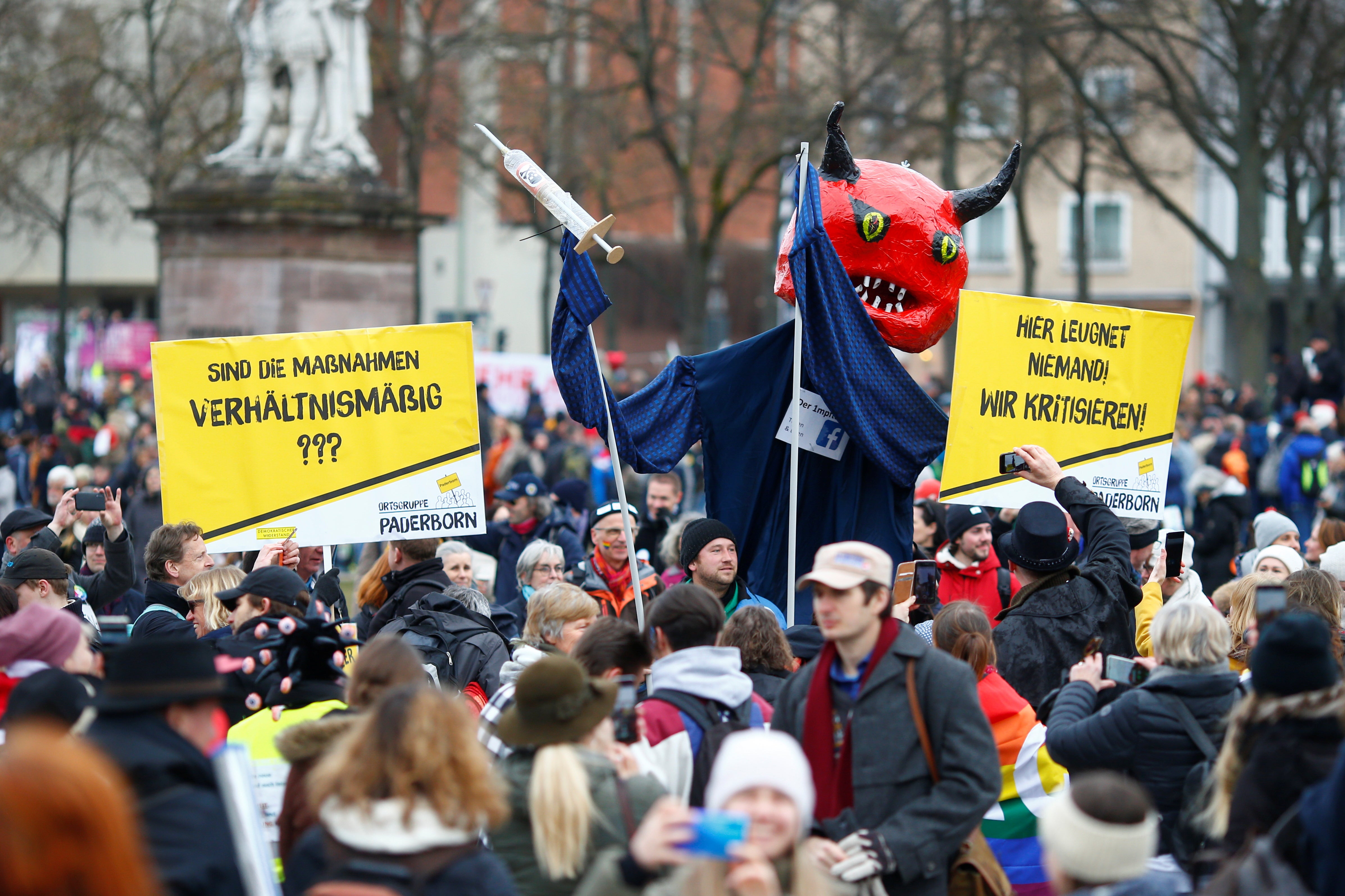 A demonstrator holds a giant puppet depicting a devil with a vaccine