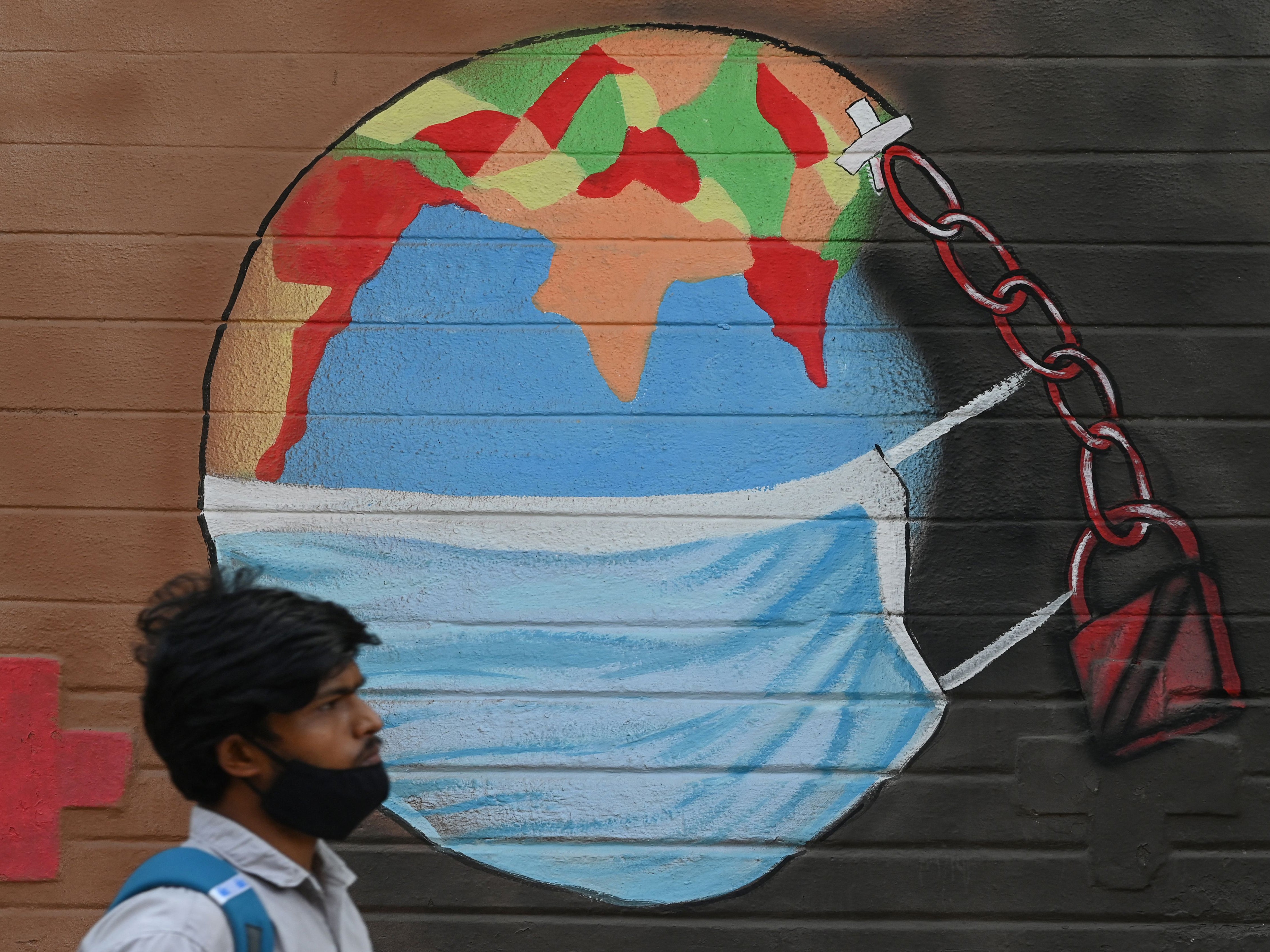 A man walks past a mural depicting the world wearing a face mask in Mumbai