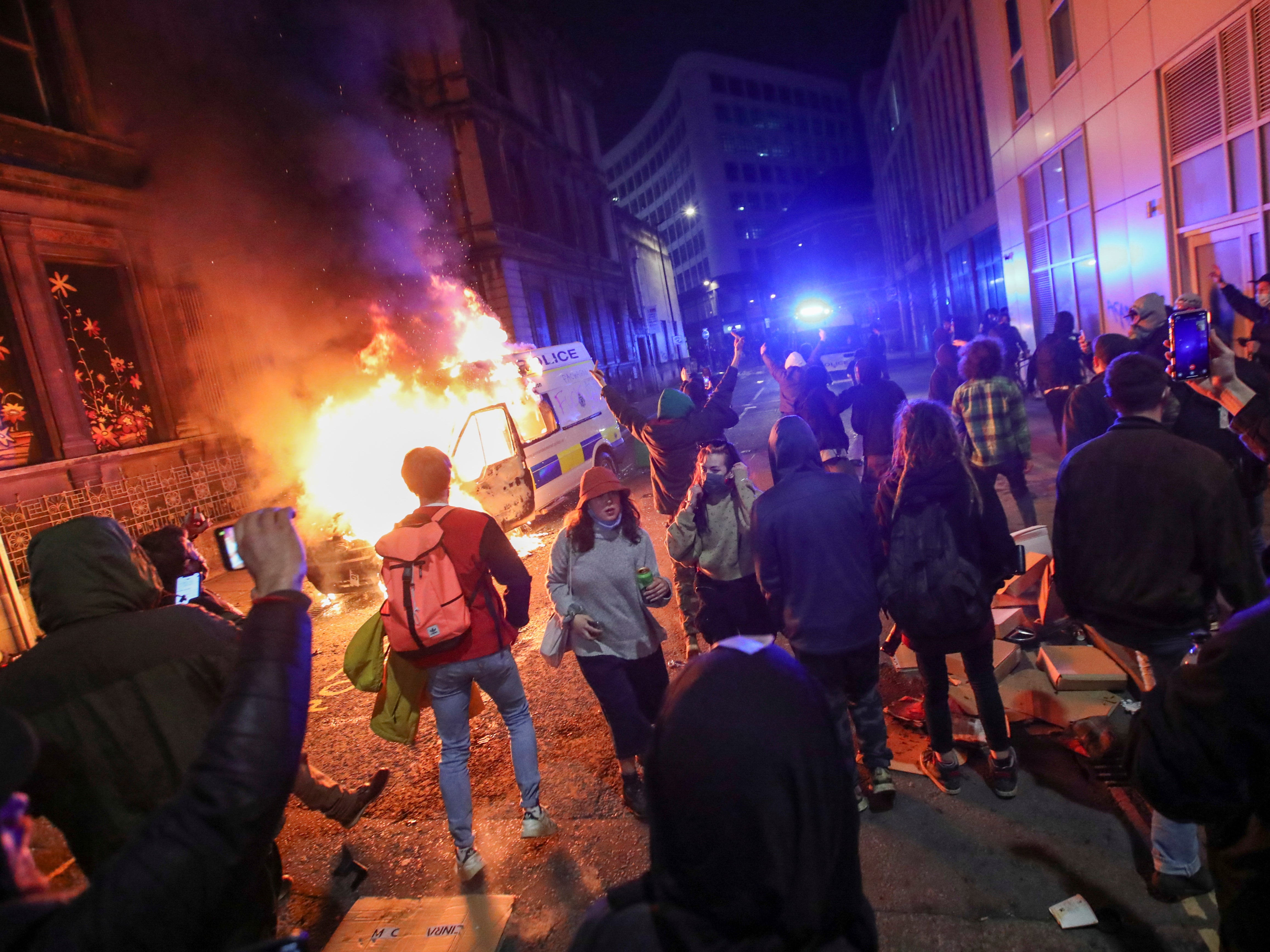 Demonstrators in Bristol stand near a burning police vehicle during a protest against the proposed policing bill