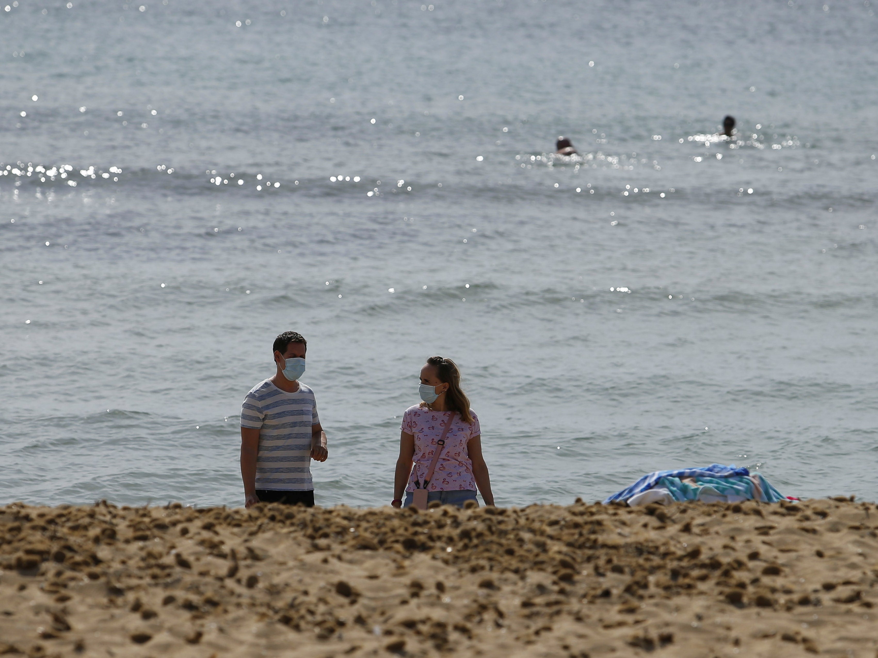 People wearing face masks walk next to the sea at Playa de Palma beach in Palma de Mallorca