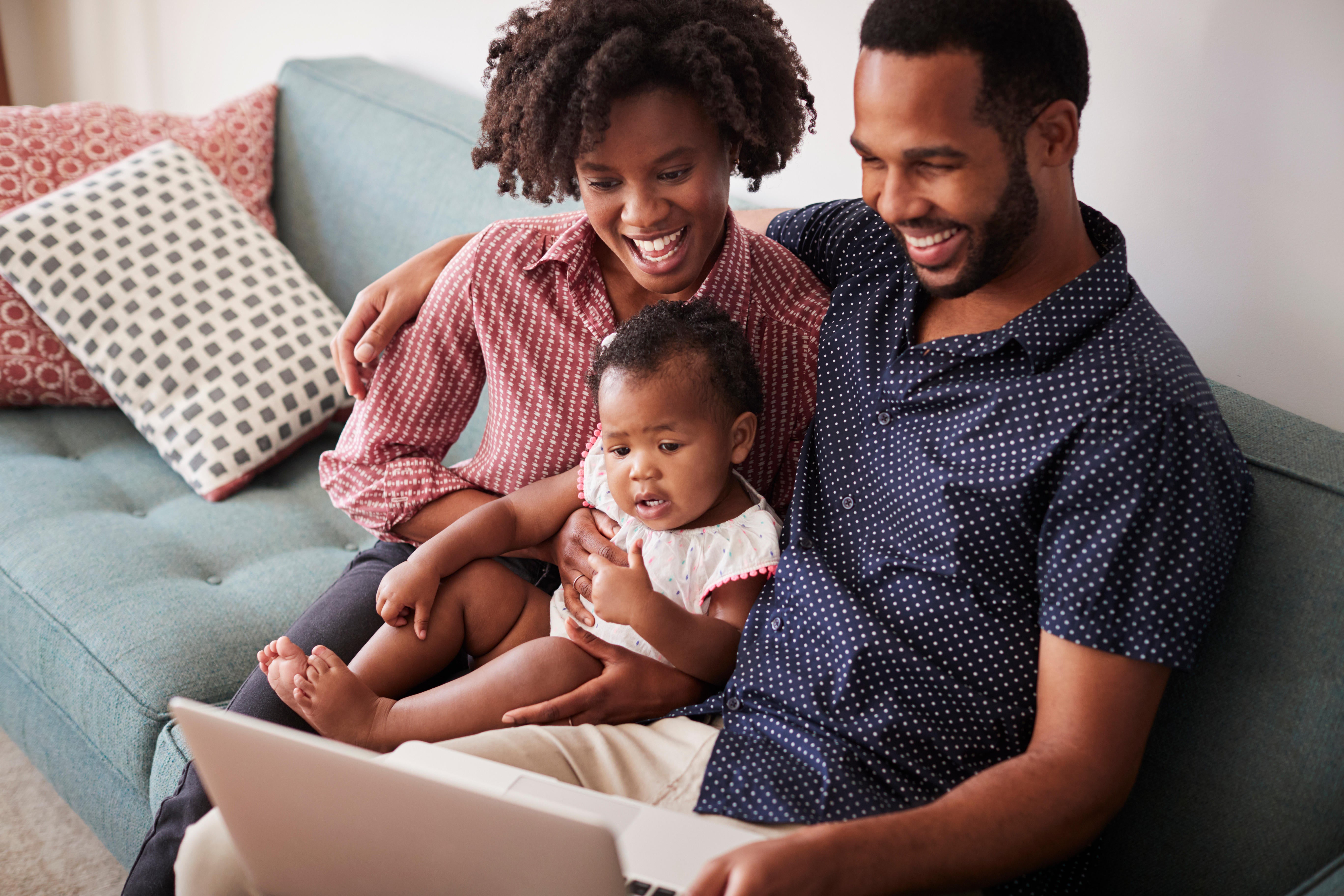 A couple and baby sat at home on the sofa, laughing