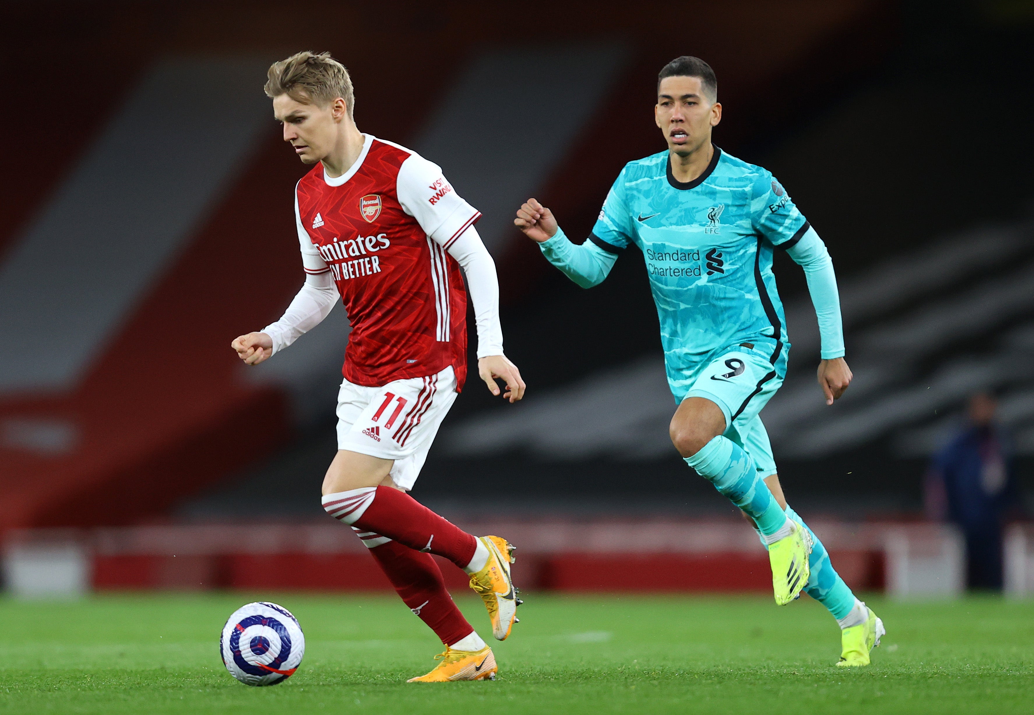 Martin Oedegaard of Arsenal runs with the ball under pressure from Roberto Firmino of Liverpool