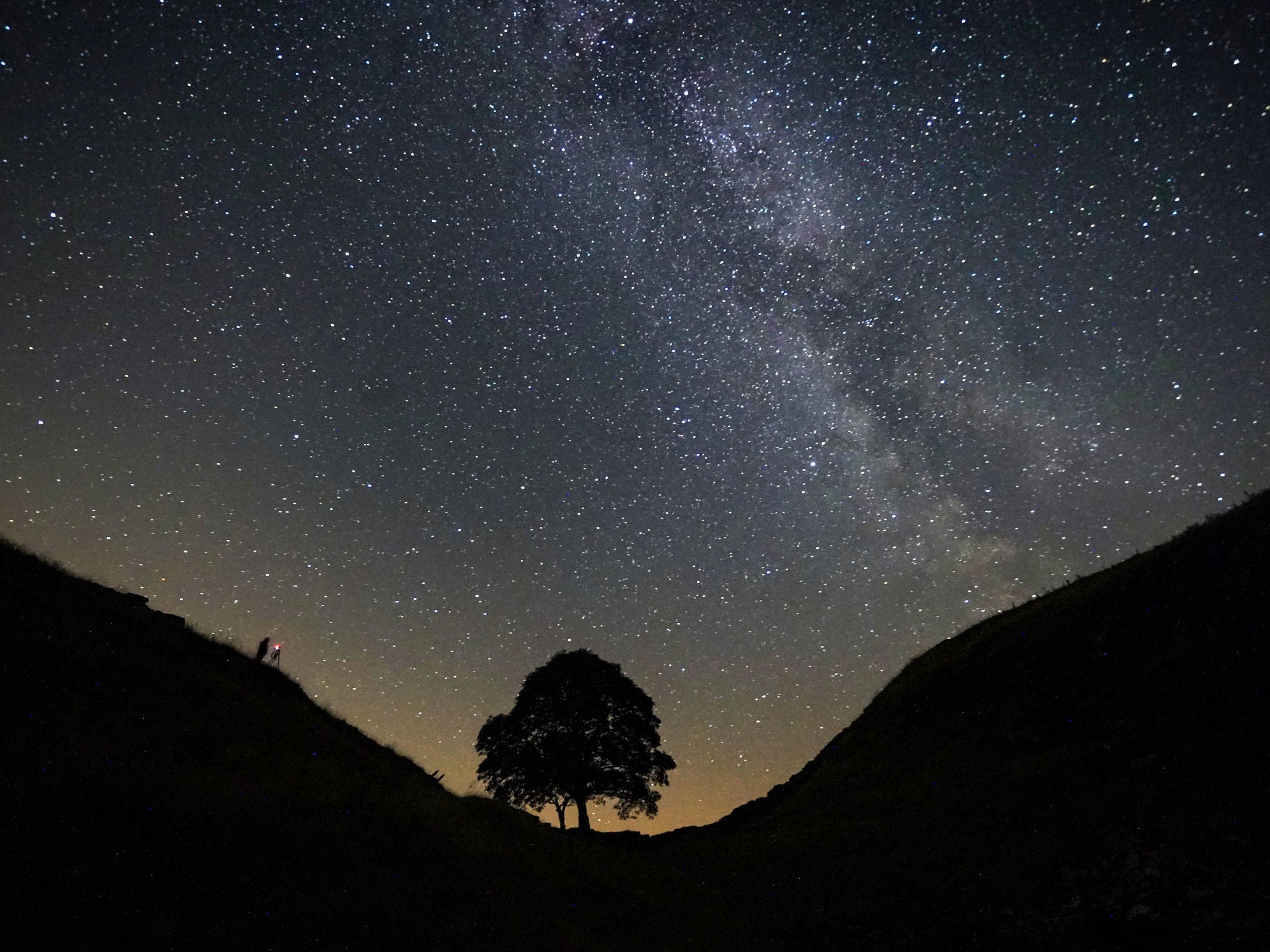 A photographer lining up a shot on a clear night under the Milky Way at Sycamore Gap on Hadrian’s Wall in Northumberland