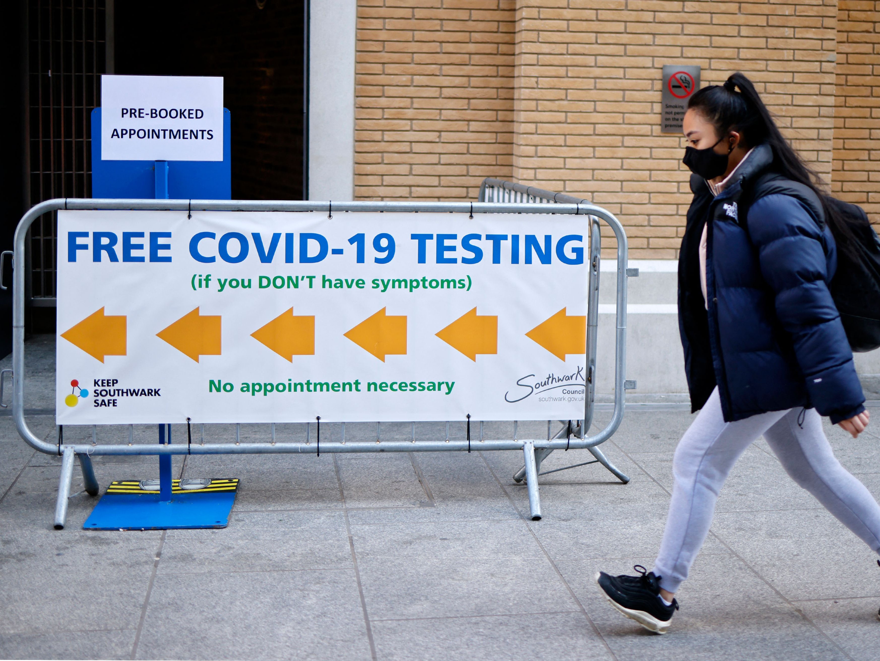 A pedestrian wearing a face covering walks past a sign directing people to a rapid lateral flow Covid-19 testing centre at London Bridge train station