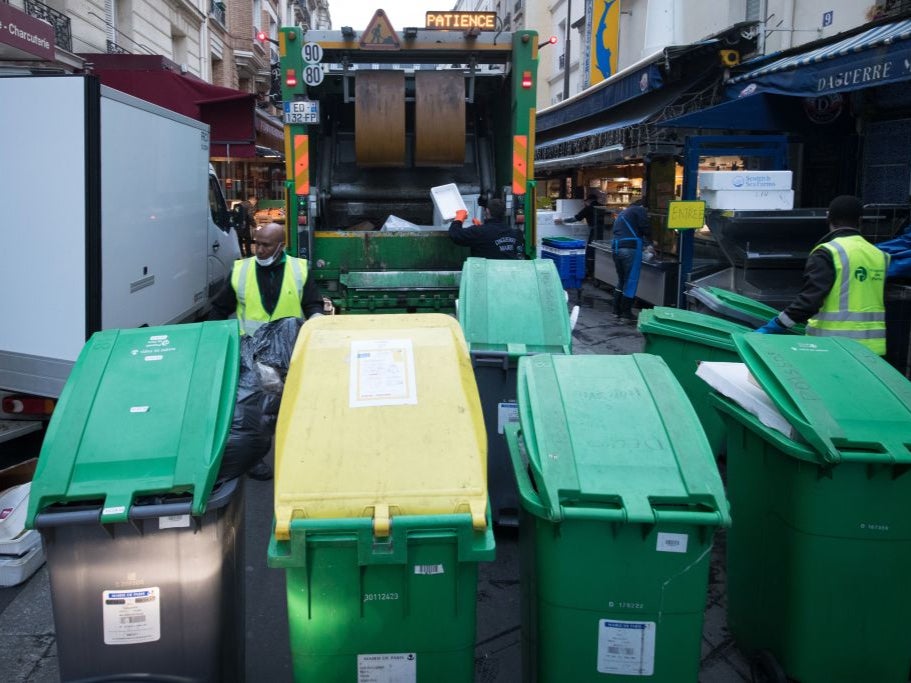 Rubbish collectors of the Paris municipality cleaning service "Proprete de Paris", wearing face masks, collect waste bins to be emptied in a garbage truck in Paris