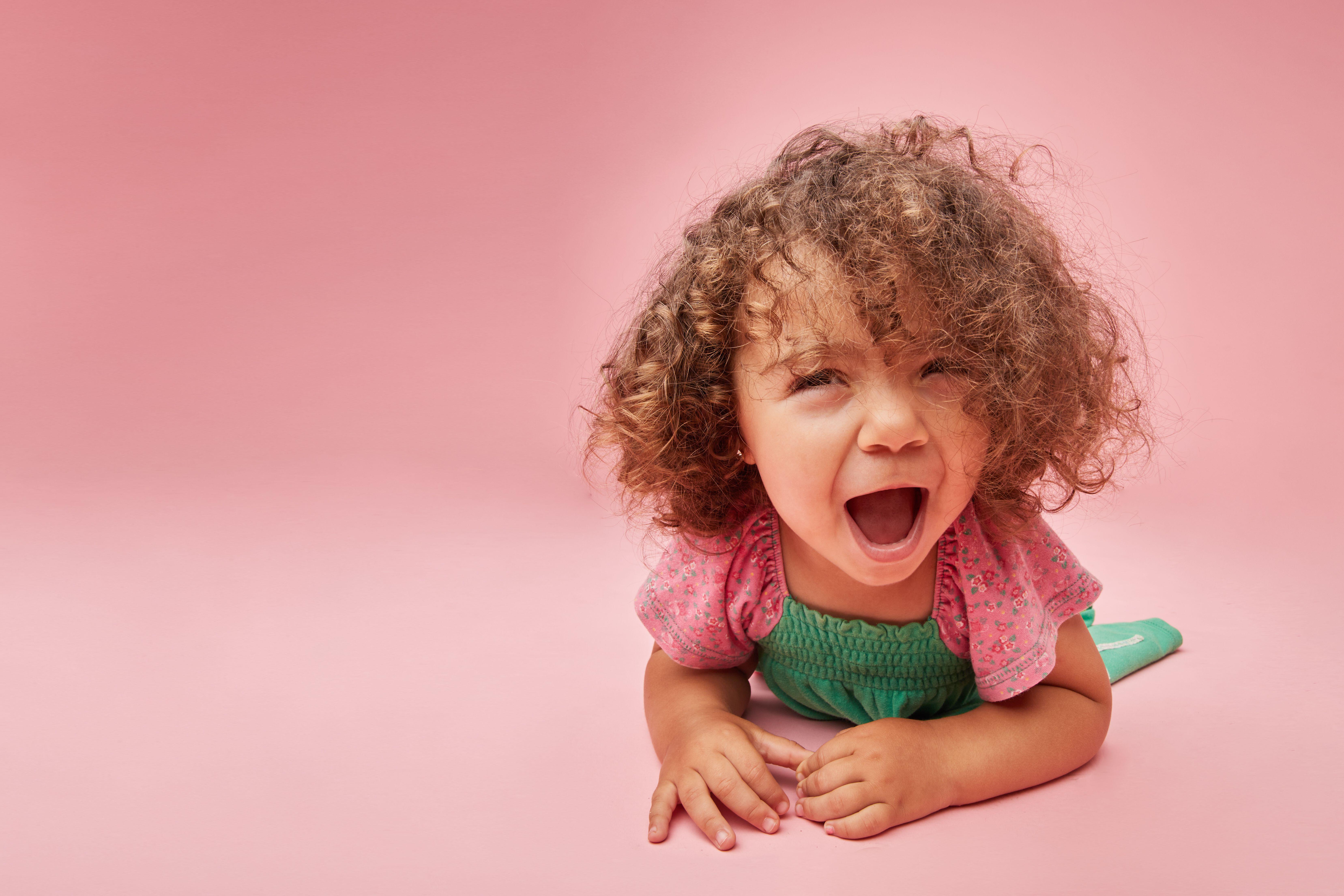 Adorable toddler child in dress with curly hair having a tantrum looking away leaning sitting on the on floor