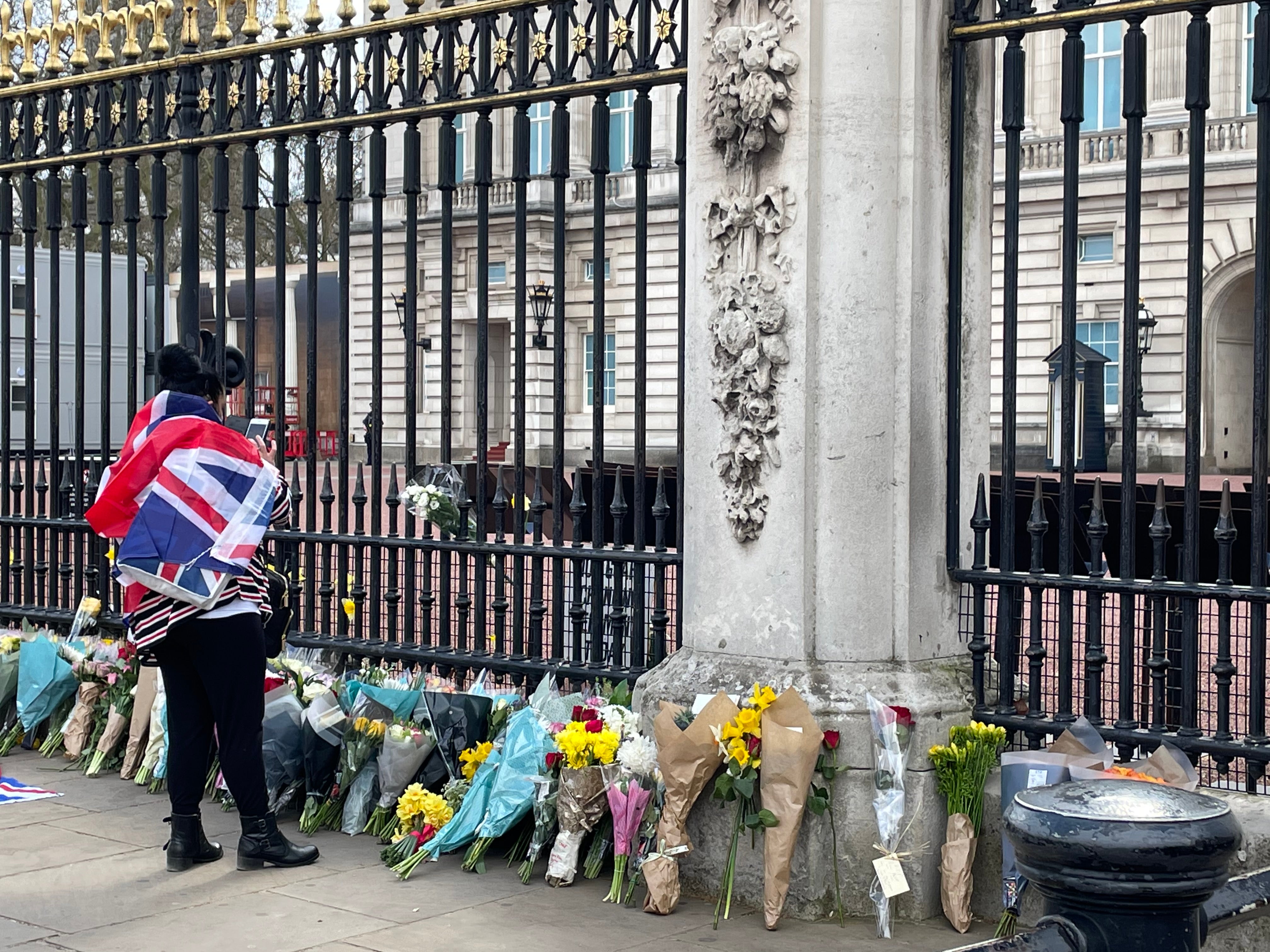 A mourner dressed in a Union Jack flag lays flowers in front of Buckingham Palace in tribute to the Duke of Edinburgh