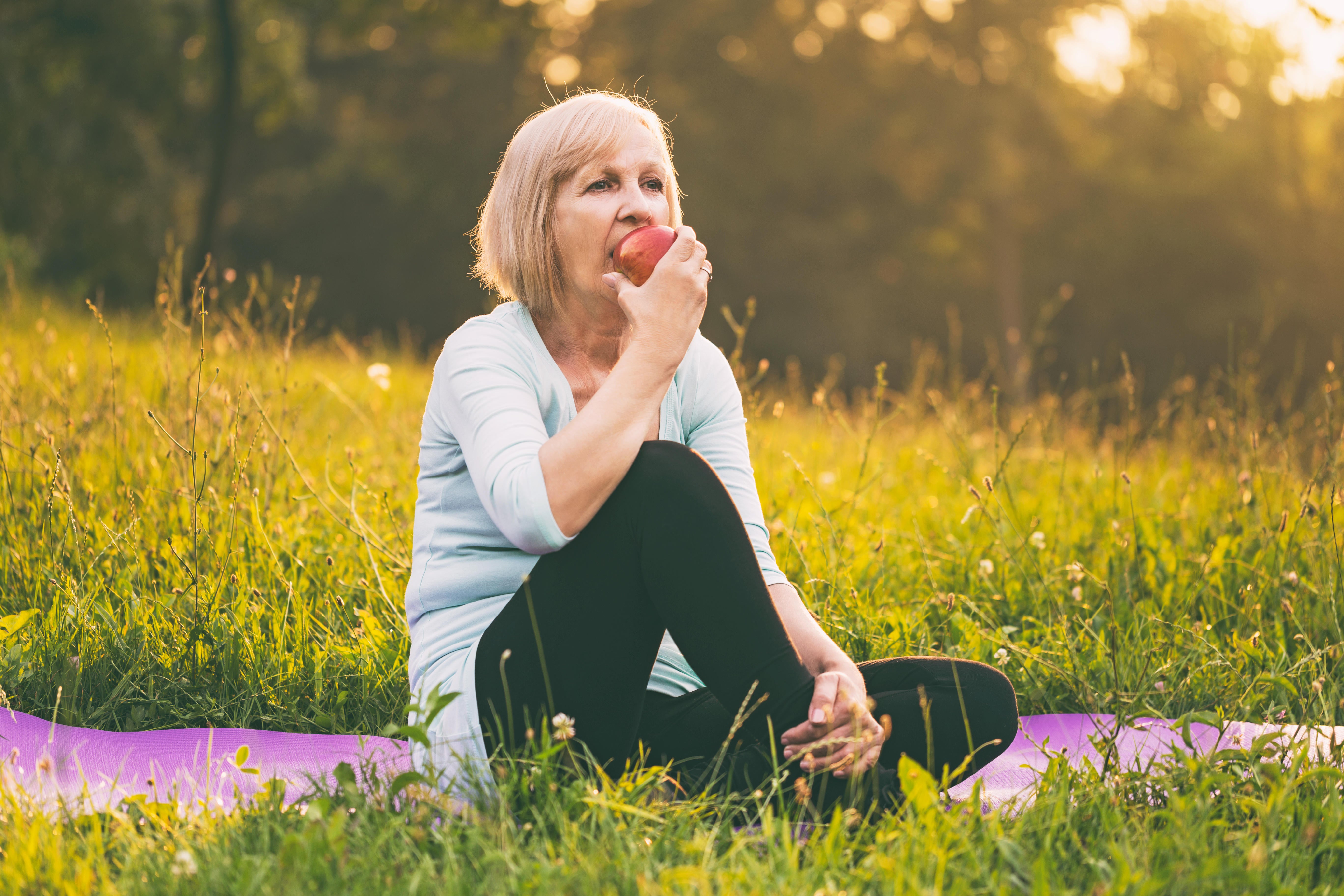 Woman sat in a meadow eating an apple