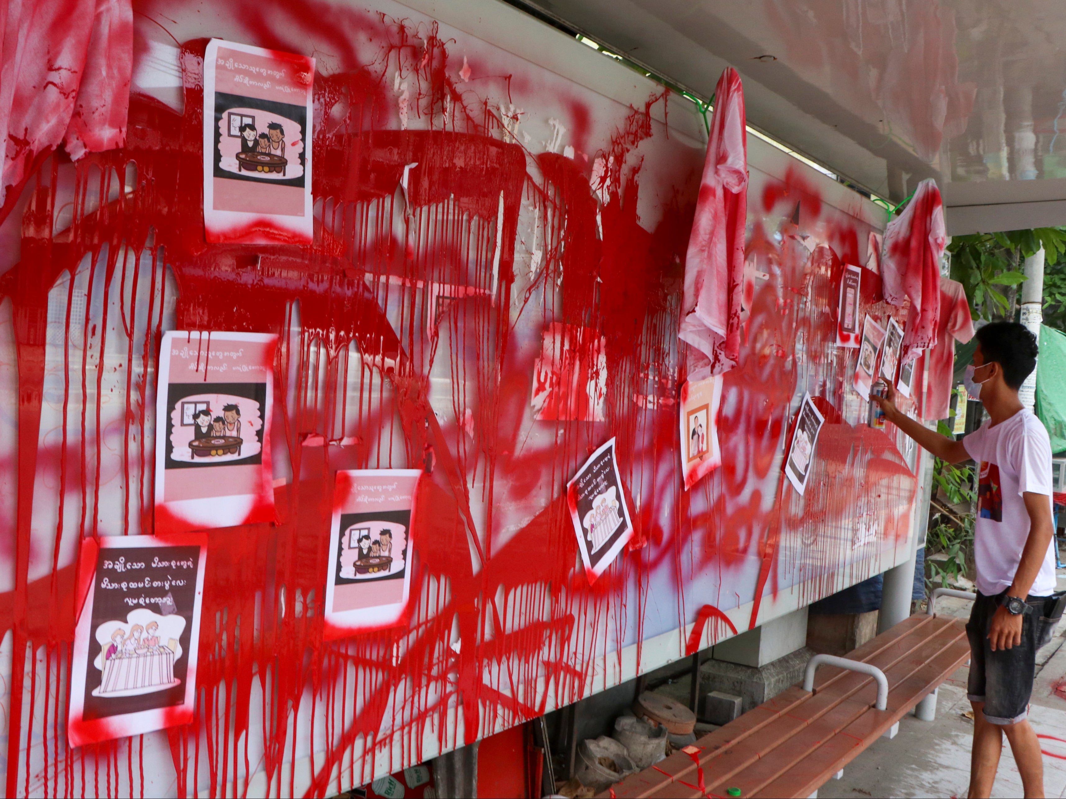 An anti-coup protester uses red paint as he writes slogans at a bus stop in Yangon, Myanmar