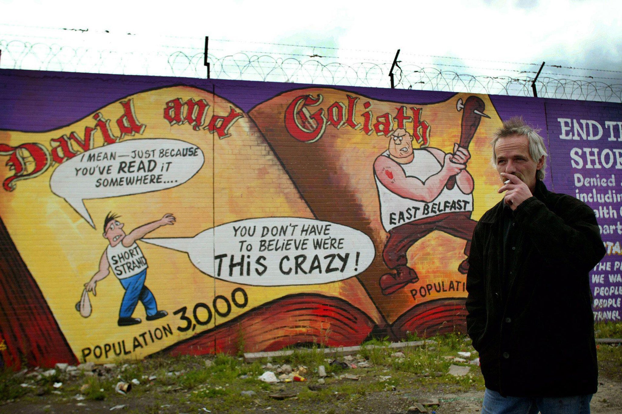 Danny Devenny stands in front of his work depicting nationalists as David and loyalists as Goliath in the Short Strand area of Belfast, July 2002