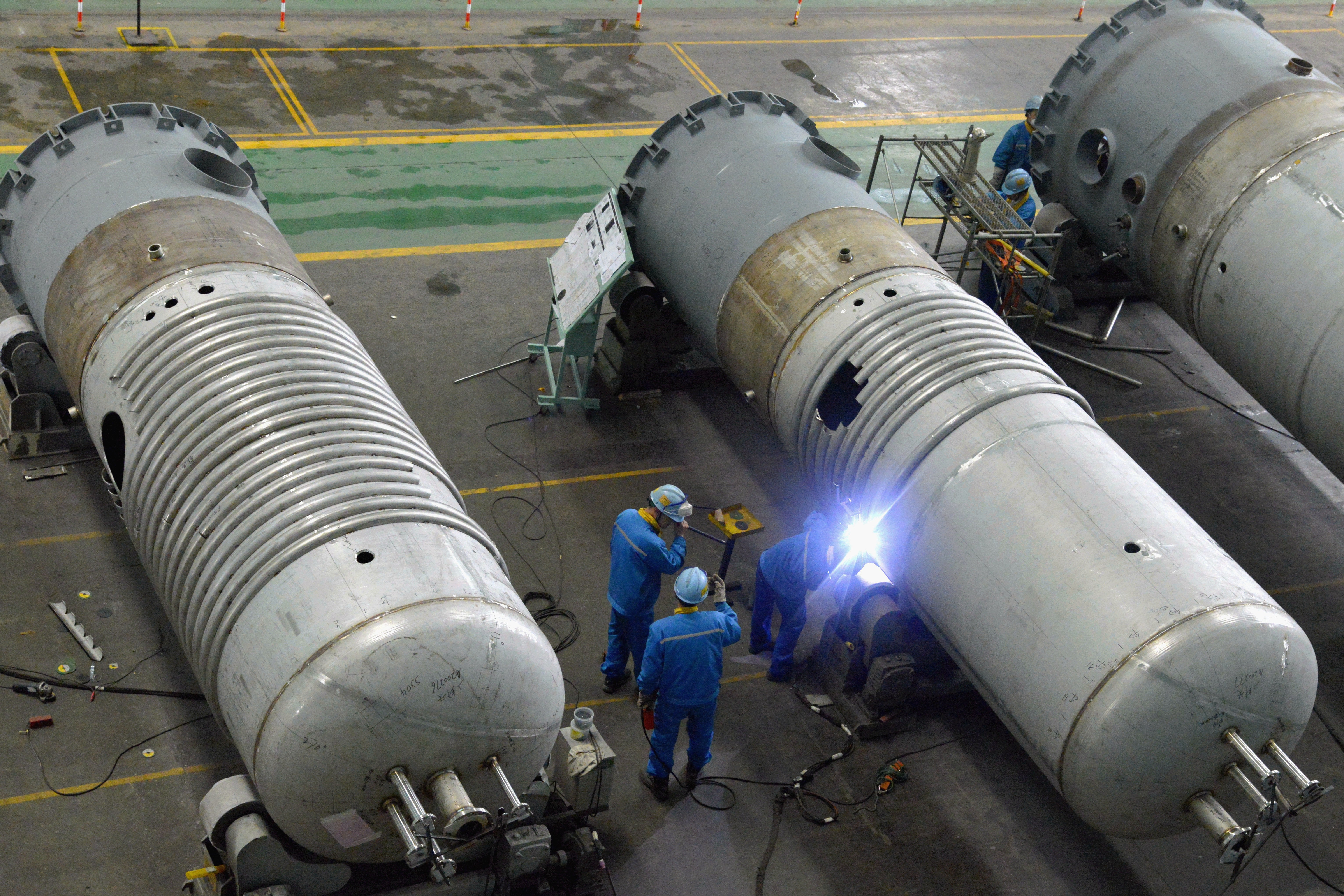 Workers weld a stainless steel oil refining tower at a factory in Jingjiang, China